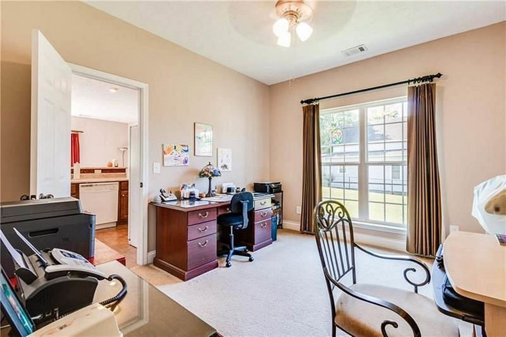 Desk with telephone and chair beside window with white curtains, wood cabinetry and drawers, light-colored walls, ceiling light fixture, hardwood floor