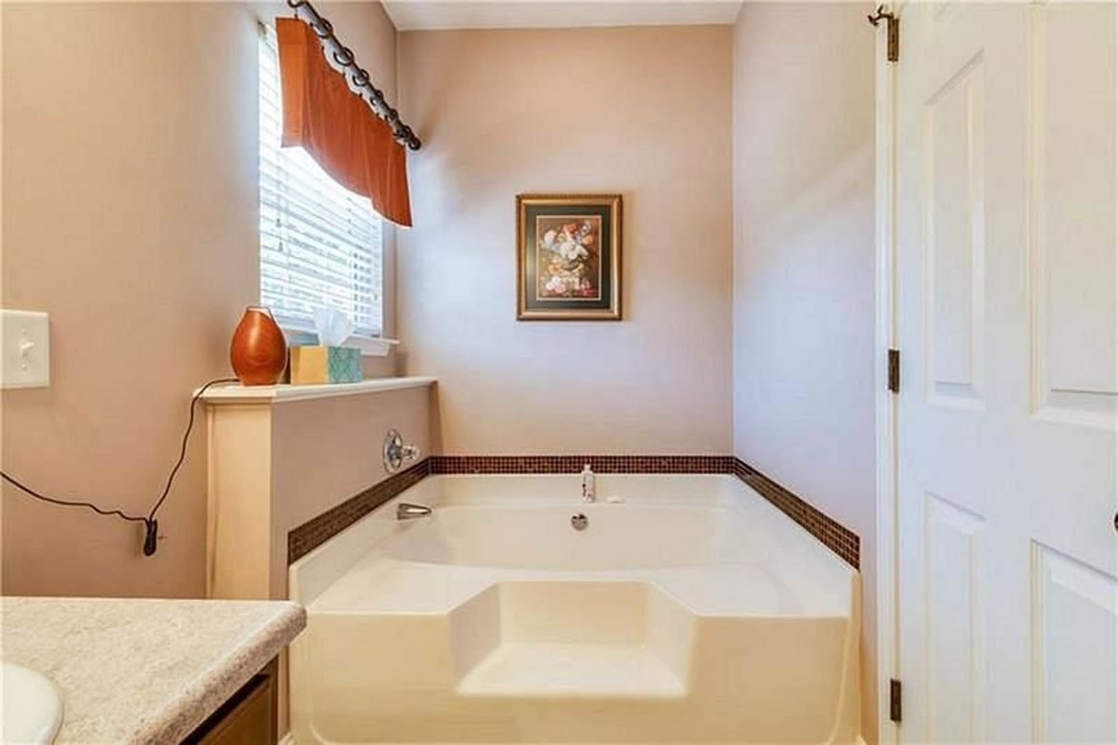Freestanding white bathtub with chrome fixtures beside a tiled wall, large mirror, and framed artwork in a modern bathroom