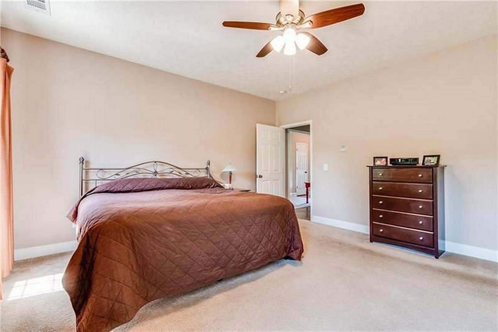 Bedroom with a bed featuring a brown blanket, white nightstand, brown dresser with white knobs, ceiling fan with light, neutral walls, and hardwood floor.