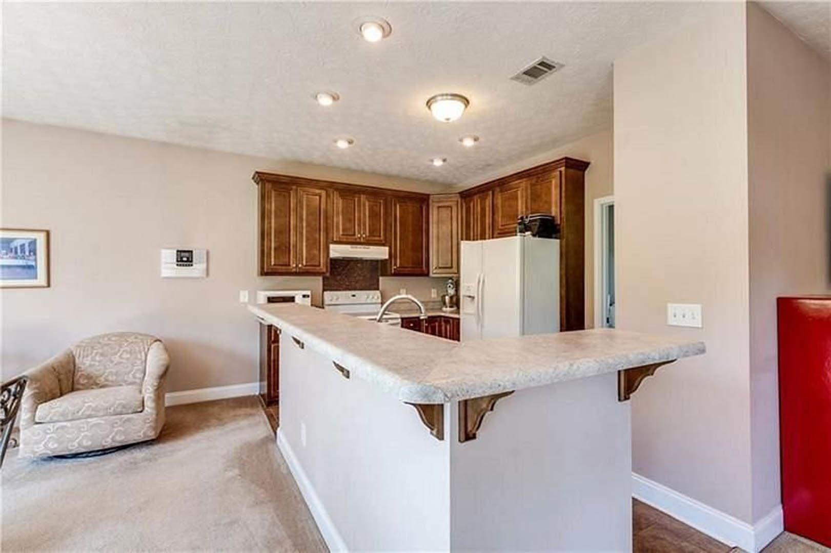 Open-concept kitchen and living room featuring a white countertop, light cabinetry, stainless steel sink, two-door white refrigerator, and a gray upholstered couch on hardwood