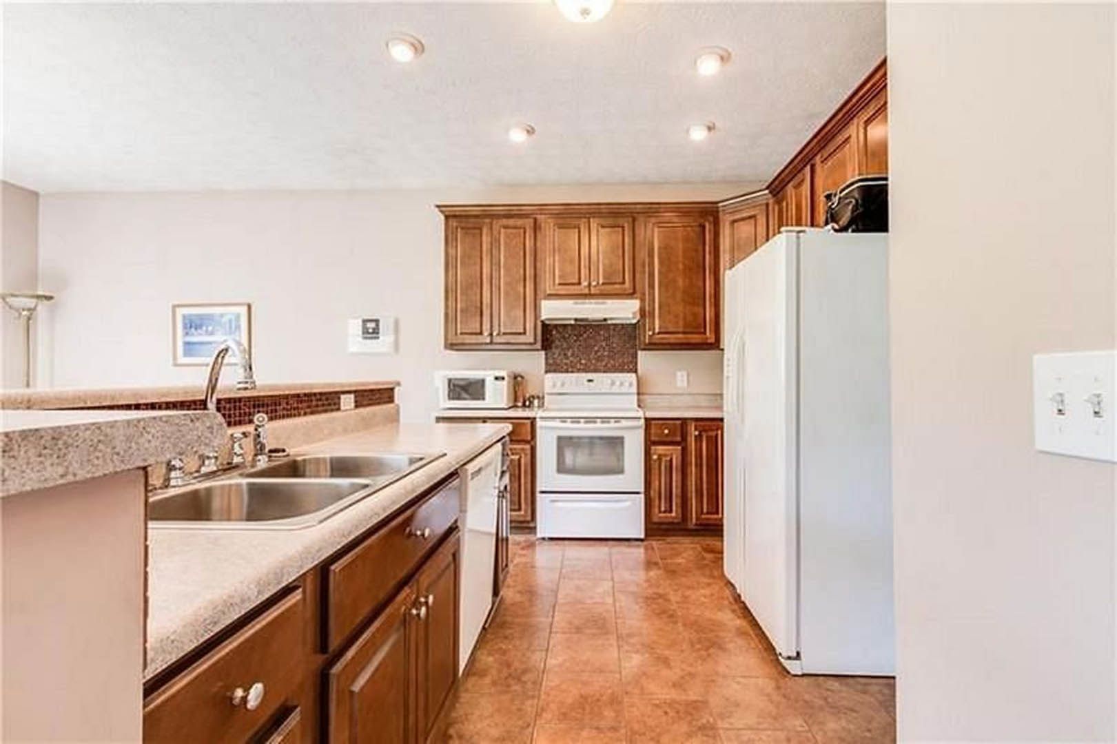 White kitchen with tile flooring, white cabinets, white stove, white refrigerator, stainless steel sink, and a window above the countertop.
