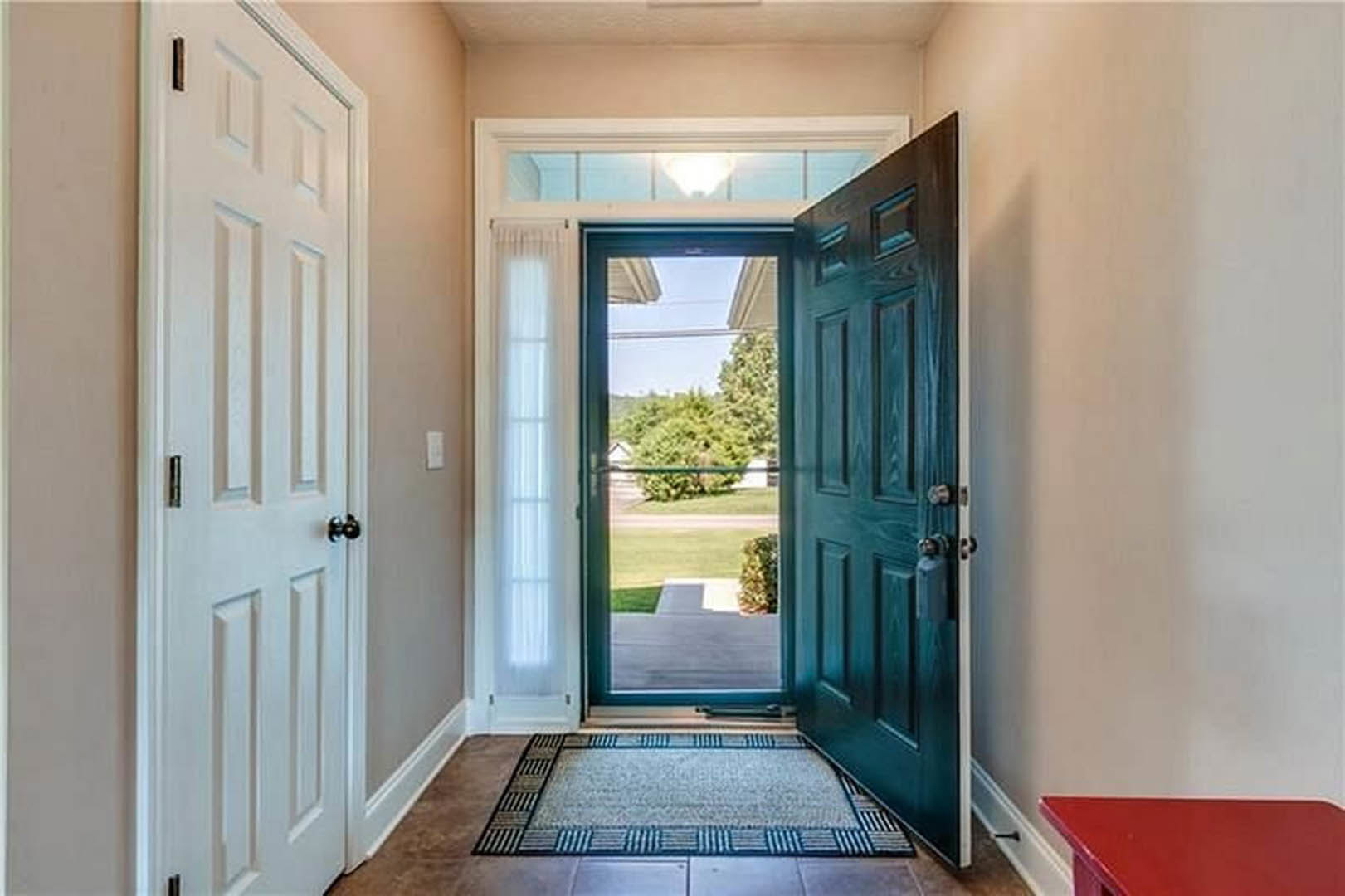 White-trimmed glass door in hallway with red accent wall, window overlooking lawn and trees, patterned rug on hardwood floor