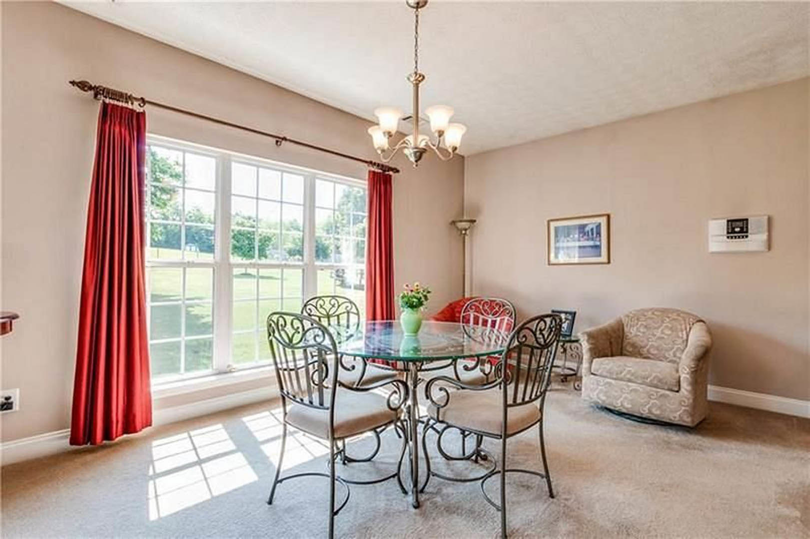 Dining room with a rectangular glass table, modern upholstered chairs, red floor-length curtains, hardwood flooring, and large windows with white trim