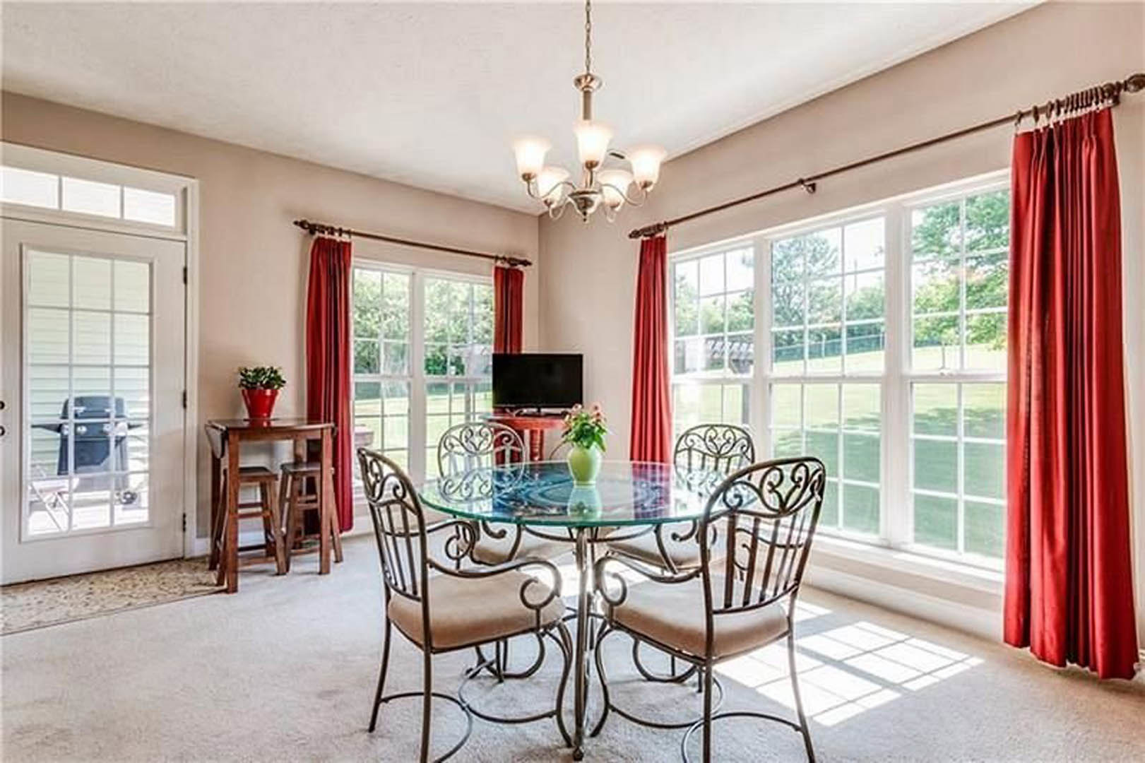 Dining room featuring a glass-top table surrounded by upholstered chairs, hardwood flooring, large window with red curtains, and neutral wall finishes