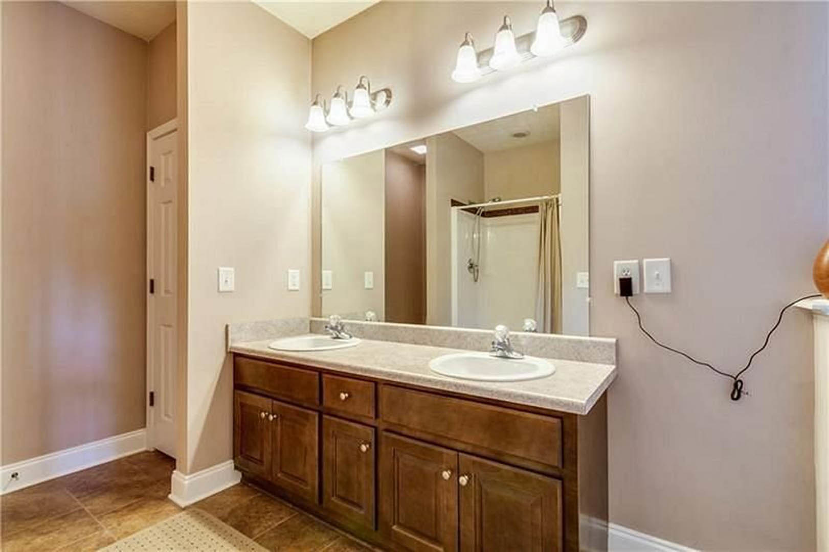 Double vanity with white sinks, wide mirror above, light wood cabinetry, chrome faucets, neutral tile backsplash, and soft overhead lighting