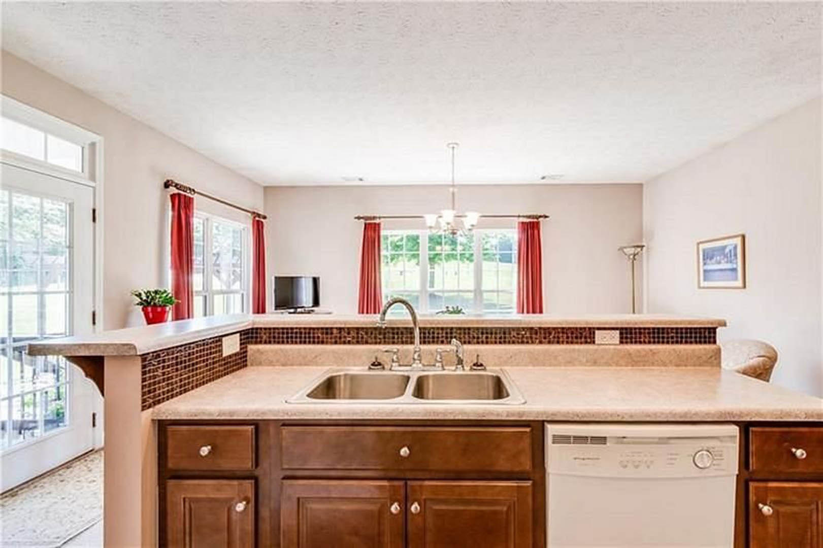 Modern kitchen with white cabinetry, stainless steel sink and dishwasher, stone countertop, chrome faucet, potted plant, and framed artwork on the wall