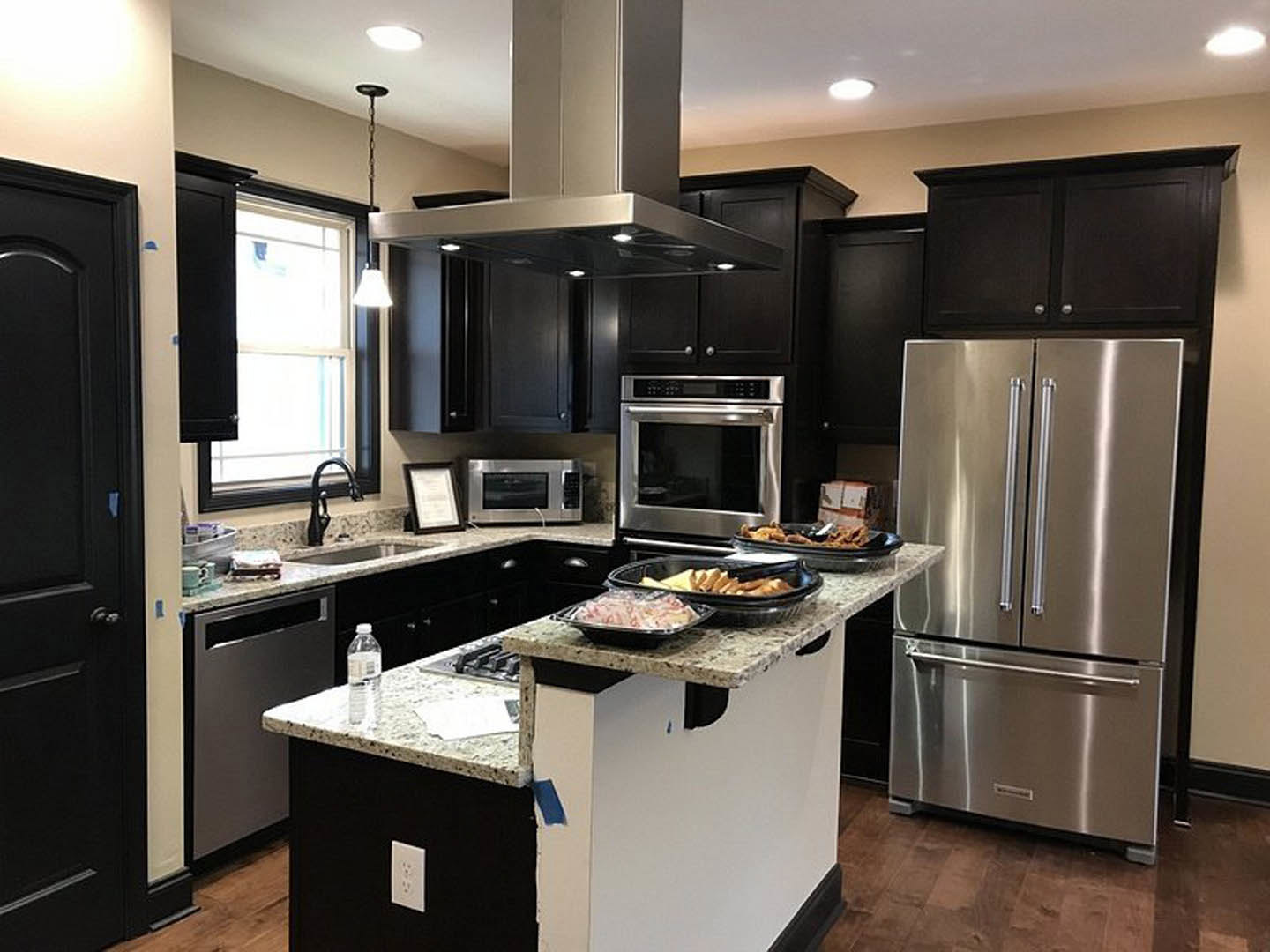 Spacious kitchen featuring a large quartz island, two-door stainless steel refrigerator, stainless steel oven with glass door, white cabinetry, and light tile backsplash