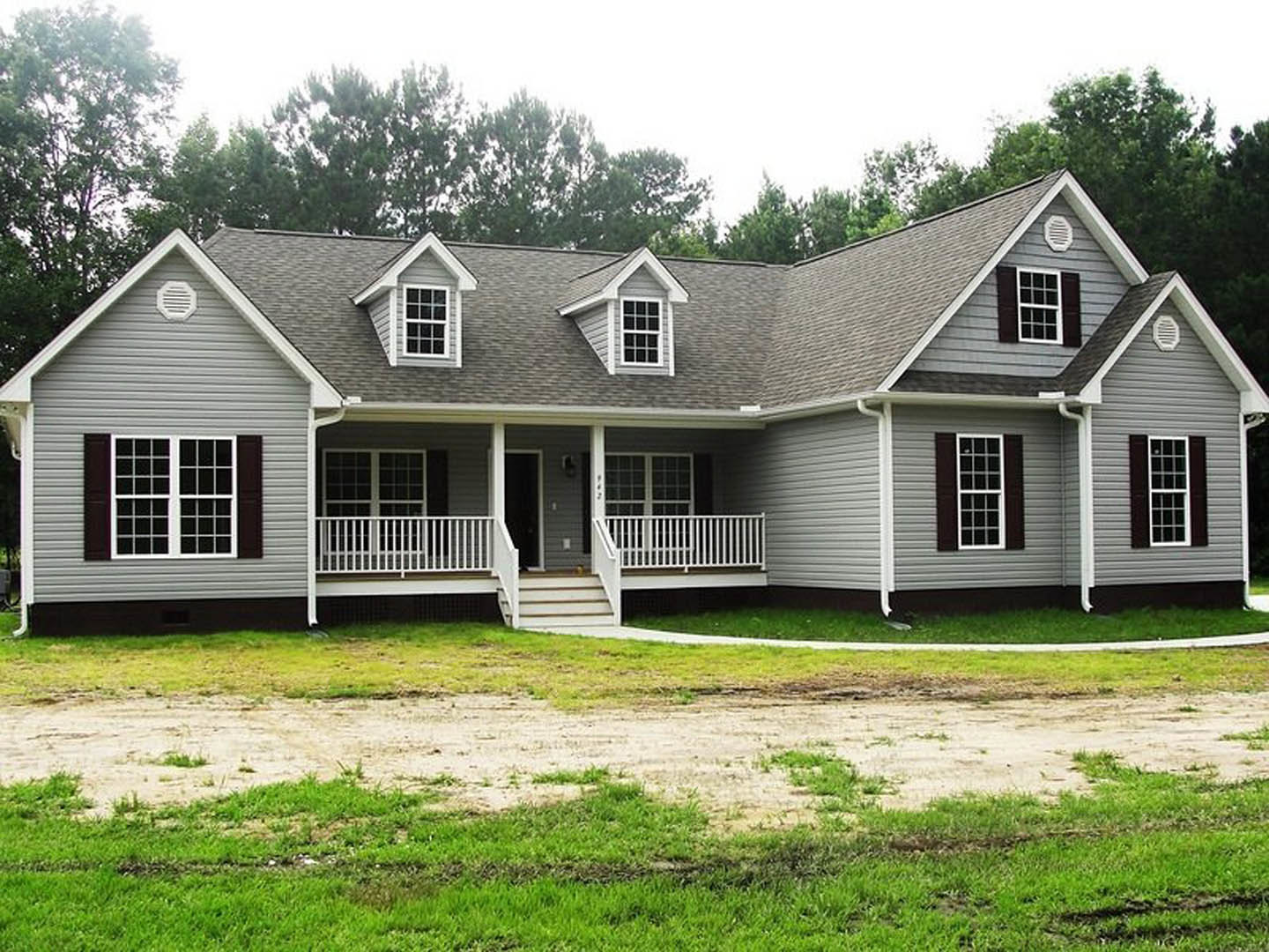 Gray-sided house with white trim, multiple windows, covered porch with white railing, concrete driveway, green lawn