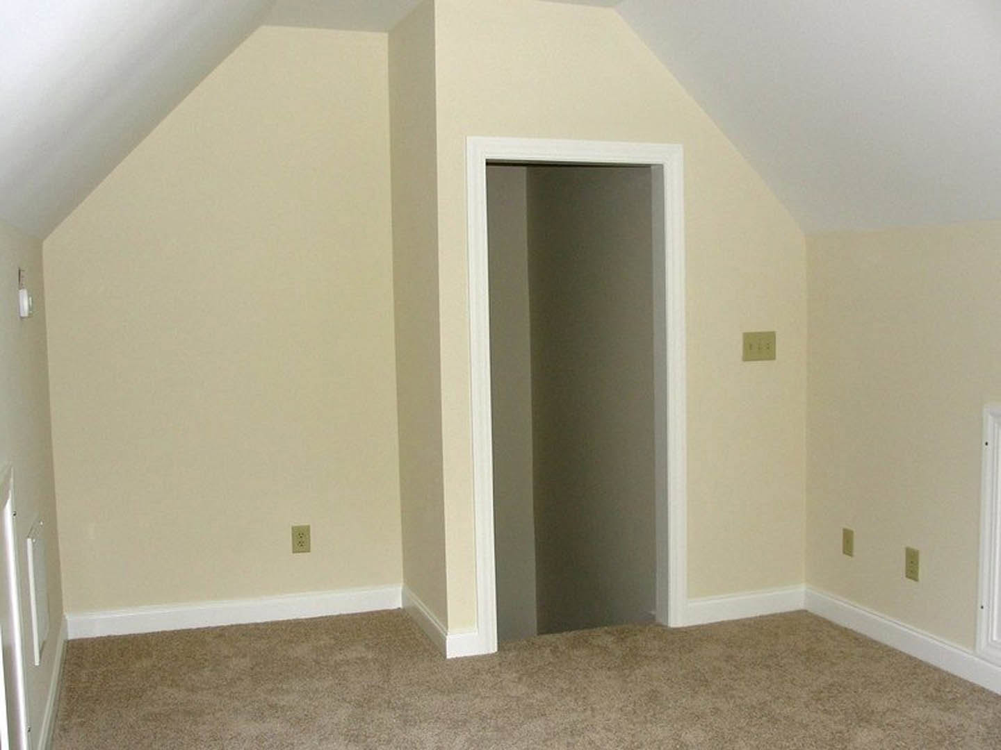 White door with matching frame opens into carpeted room, white walls and ceiling, light switch visible on wall, simple molding along ceiling.