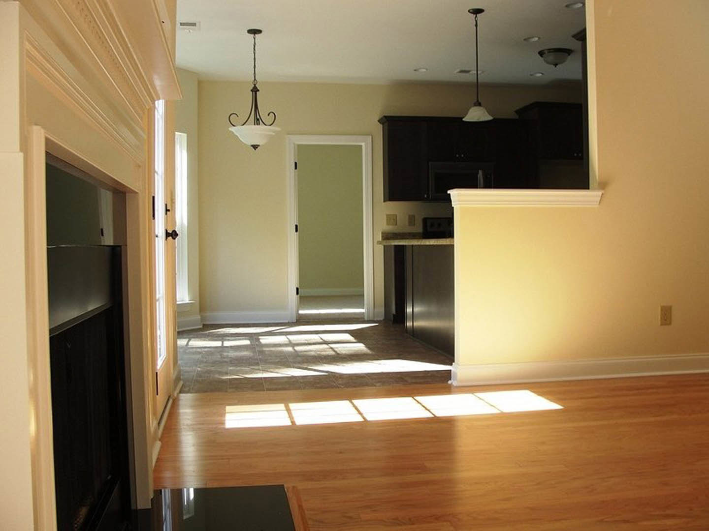 Open concept living room with wooden laminate flooring, modern kitchen cabinetry, dining area, white door frame against a green accent wall, close-up chandelier, and natural light