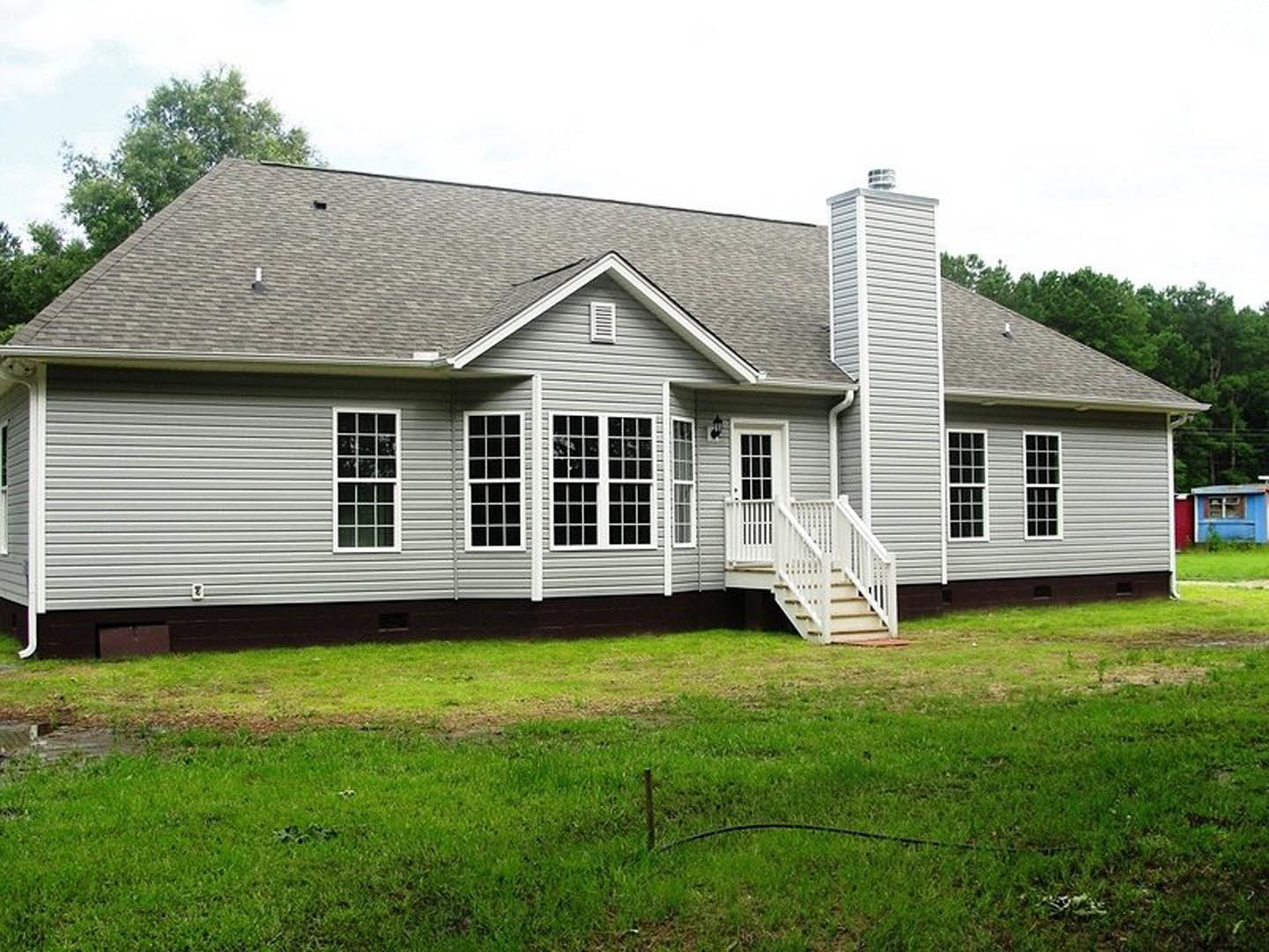 Grey siding with white trim, multi-pane window, white porch and railing, green lawn in front of custom home
