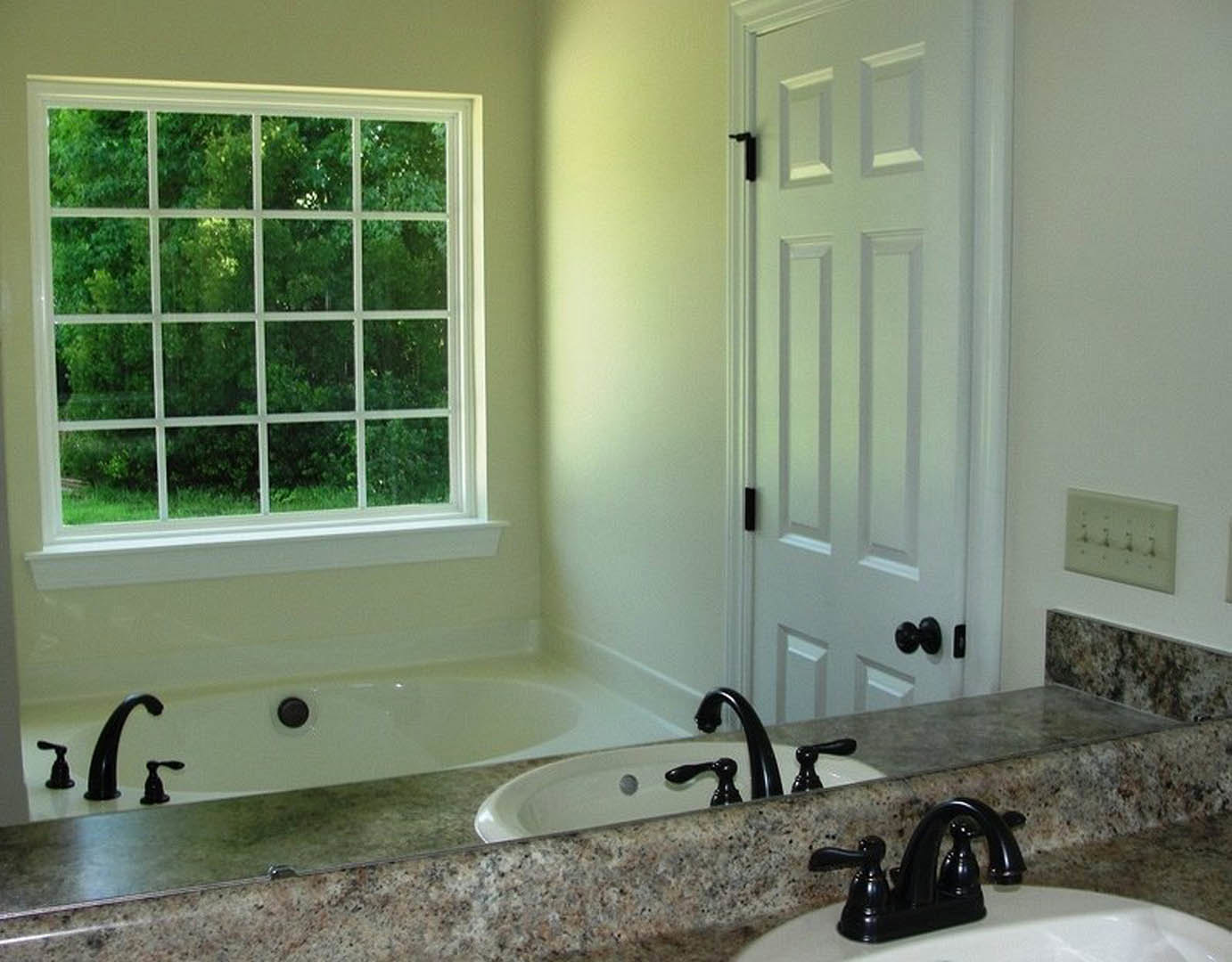 Modern bathroom featuring a freestanding white bathtub, black faucet on a white countertop sink, tiled walls, and a window with multiple square panes.