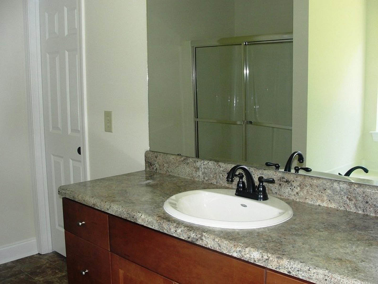 Marble countertop with white sink and black faucet, glass shower door with metal frame, tiled walls