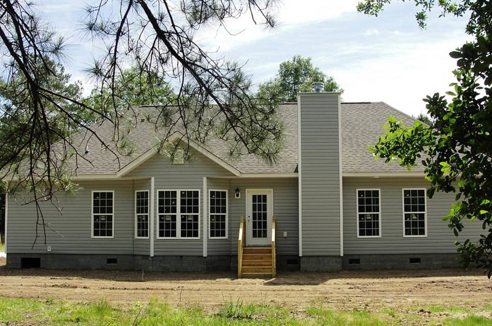 Wide front porch with wooden stairs, multi-pane windows, gray siding, and grassy yard