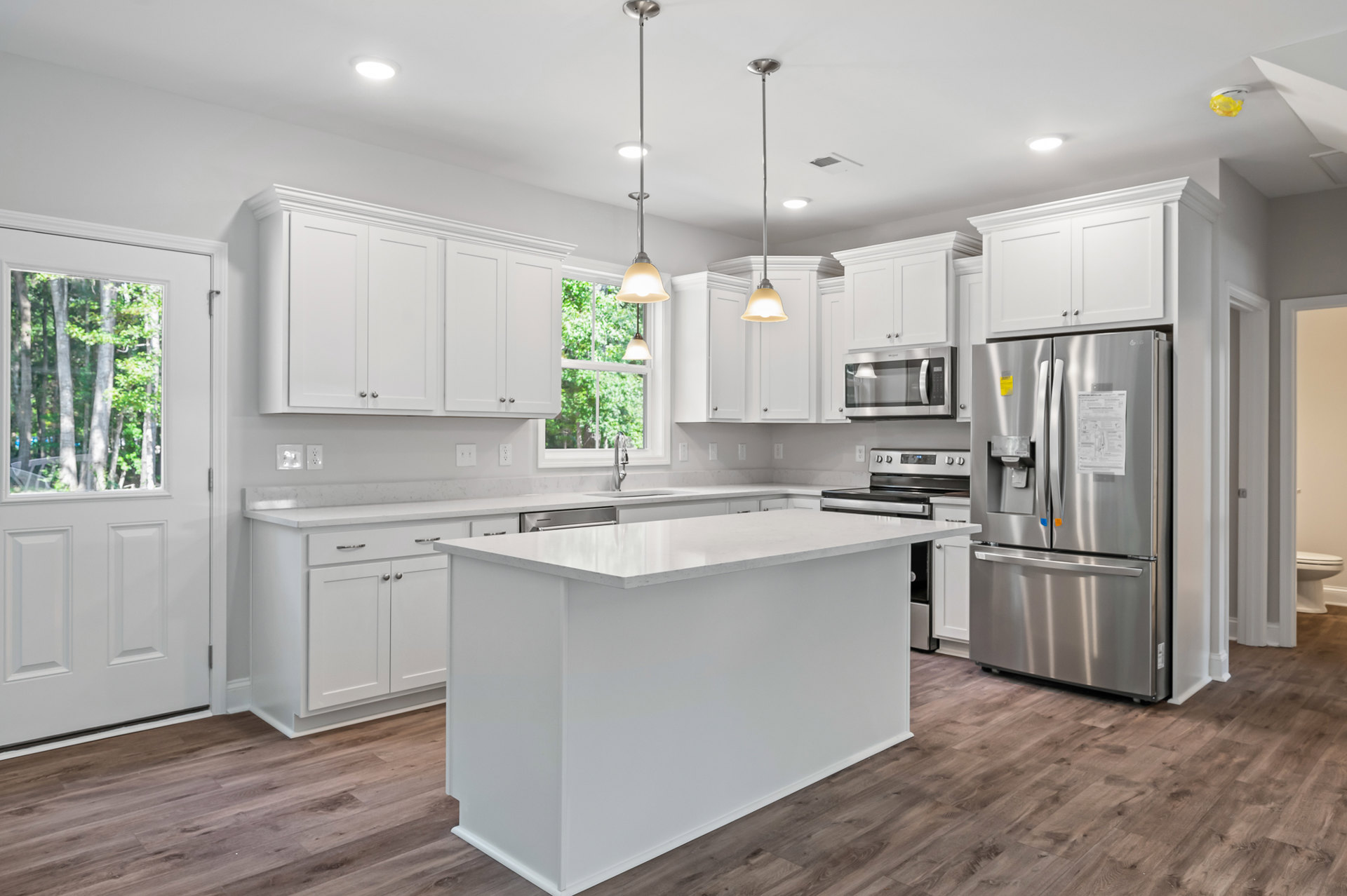White kitchen with shaker cabinets, stainless steel refrigerator, wood flooring, white island, built-in microwave, and ceiling light fixture.