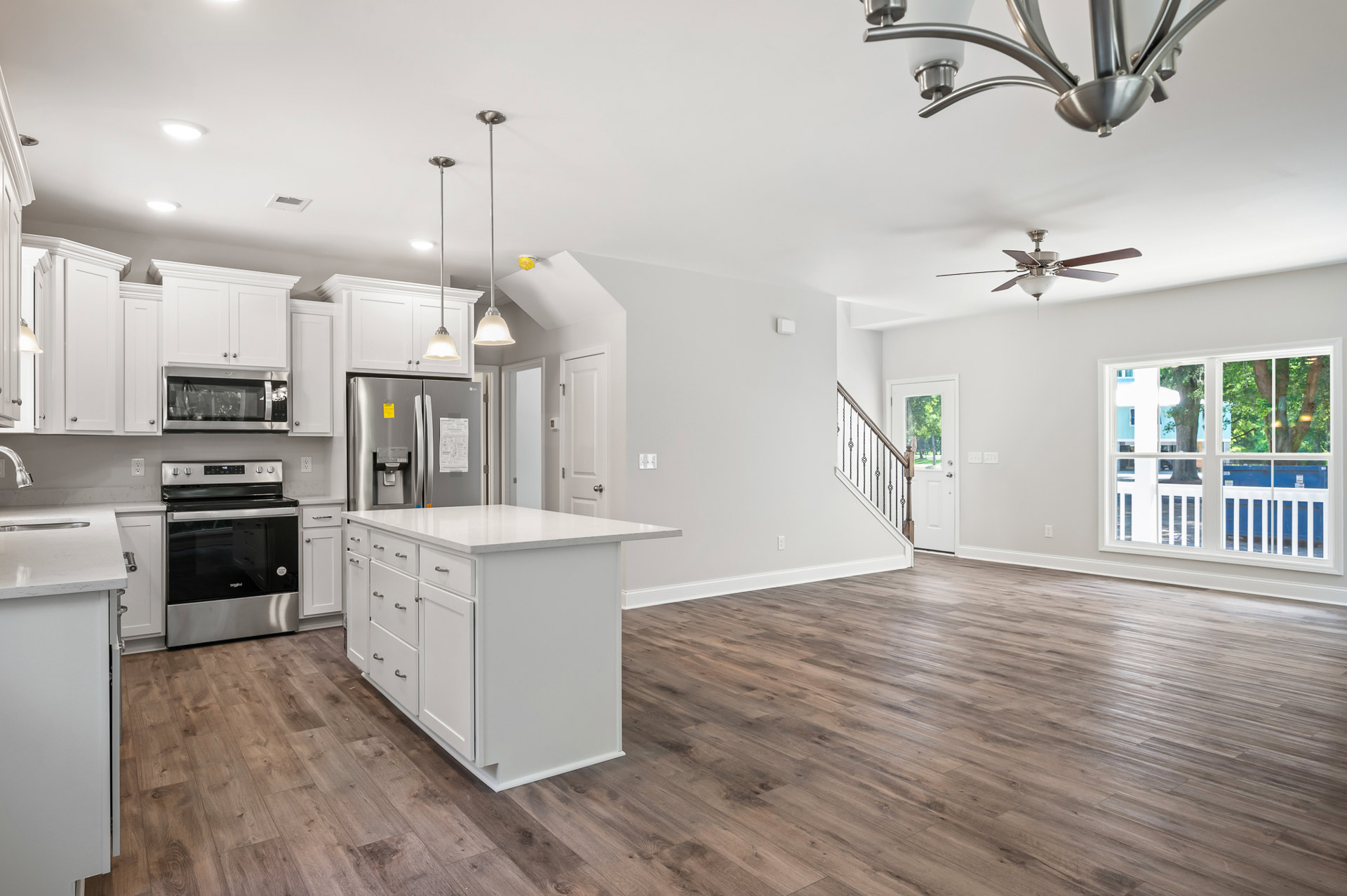 Open-concept kitchen and living room featuring hardwood floors, white kitchen island with drawers and cabinets, stainless steel stove and microwave, metal light fixture, large