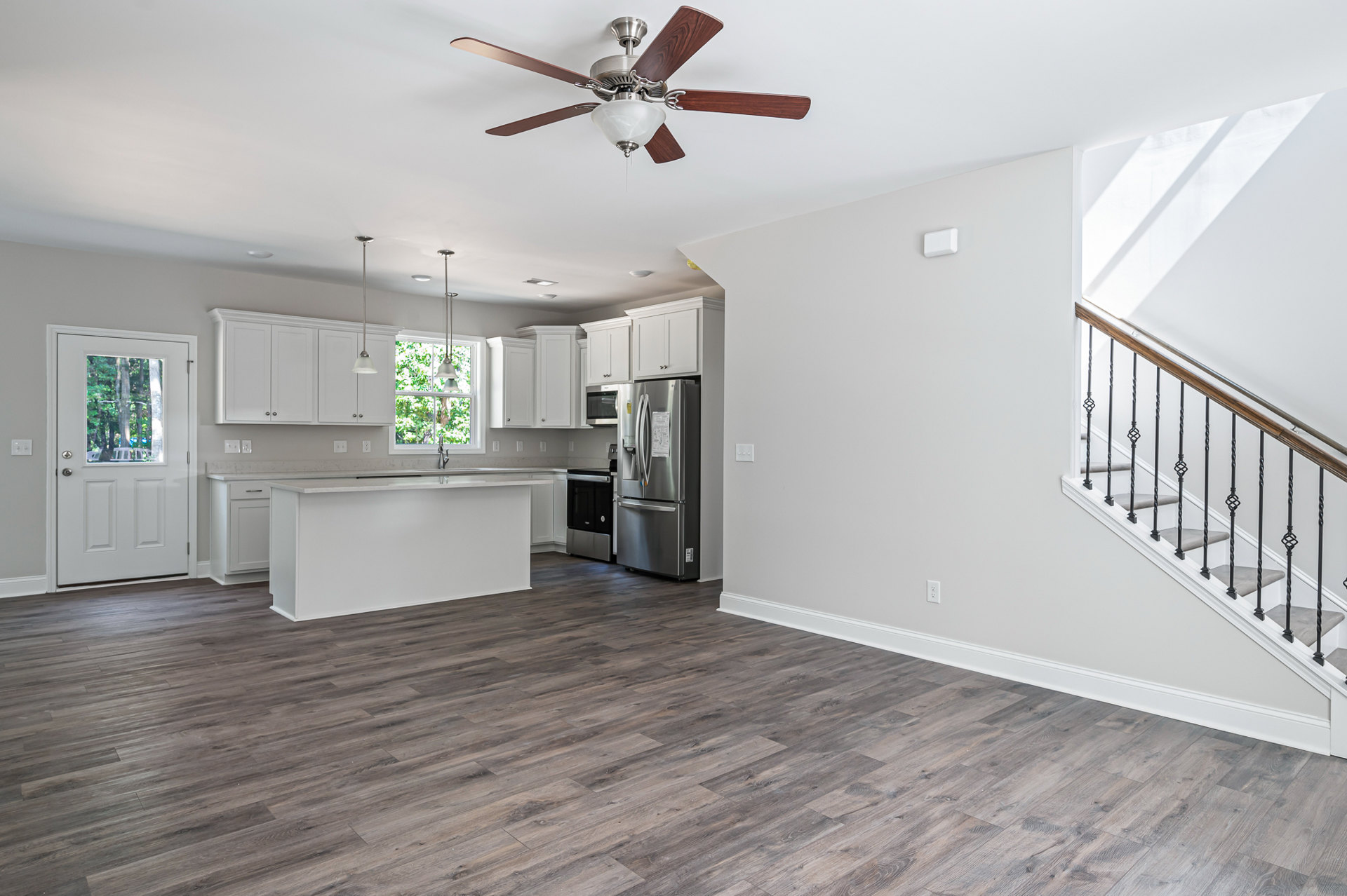 Open kitchen and dining area featuring laminate wood flooring, white cabinetry, stainless steel refrigerator, white countertop with silver barstools, ceiling fan with light