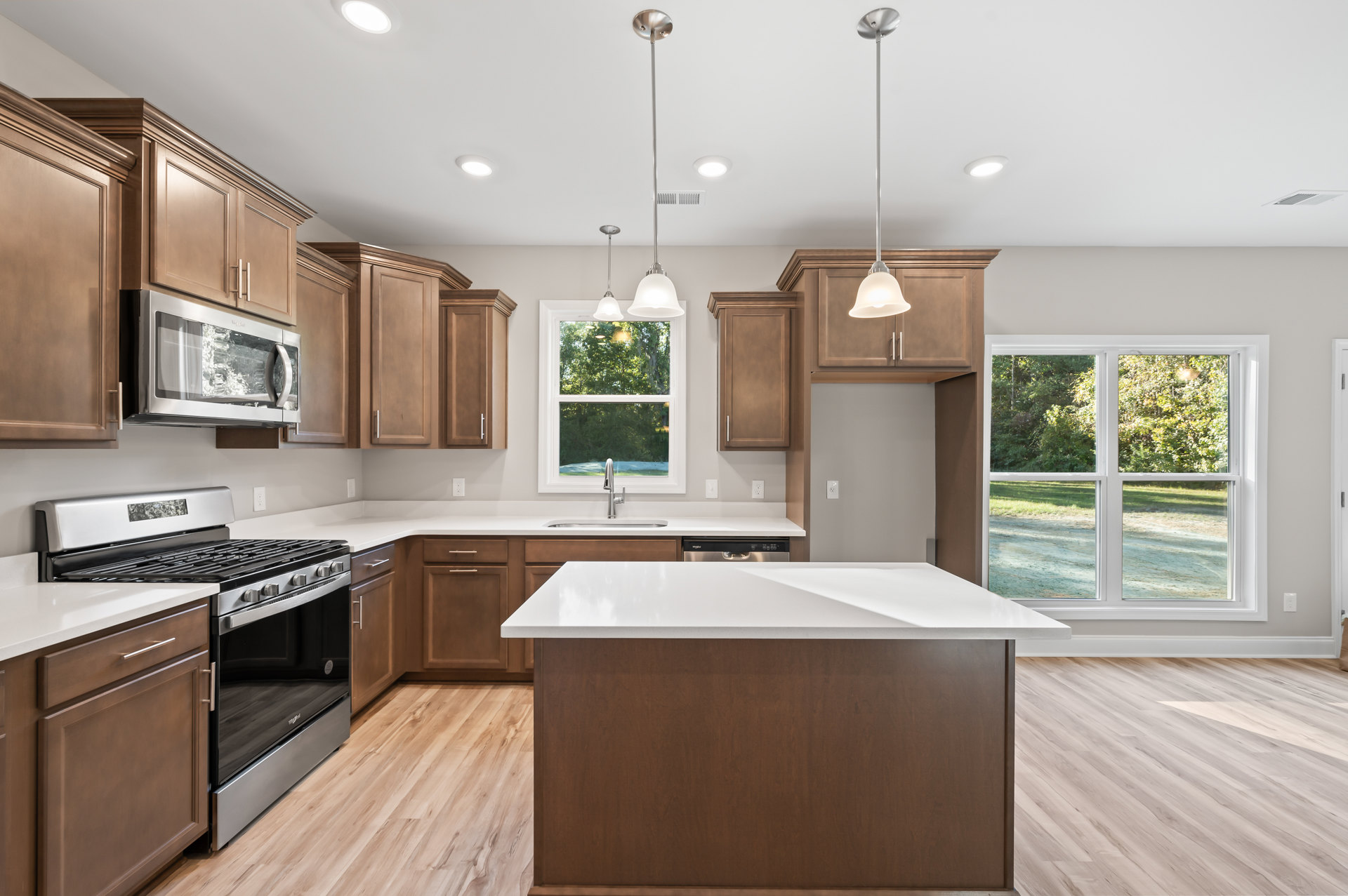 Spacious kitchen featuring a large island with white countertop and brown wood surface, stainless steel stove and oven, silver microwave with glass door, cabinetry, pendant light