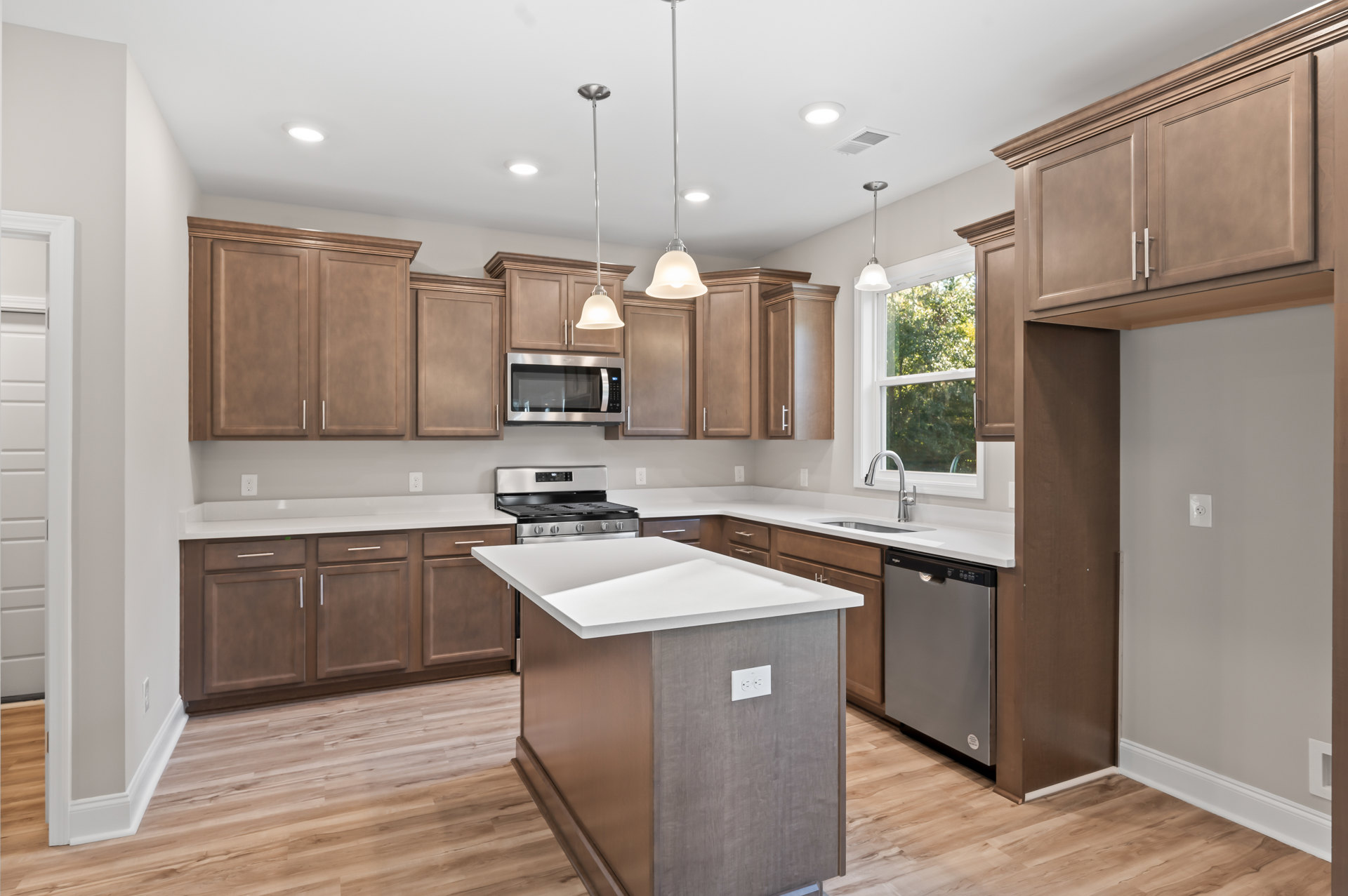 Open kitchen featuring a central island with a white countertop, stainless steel stove, built-in microwave, white cabinetry, light wood flooring, and a white pendant light fixture.