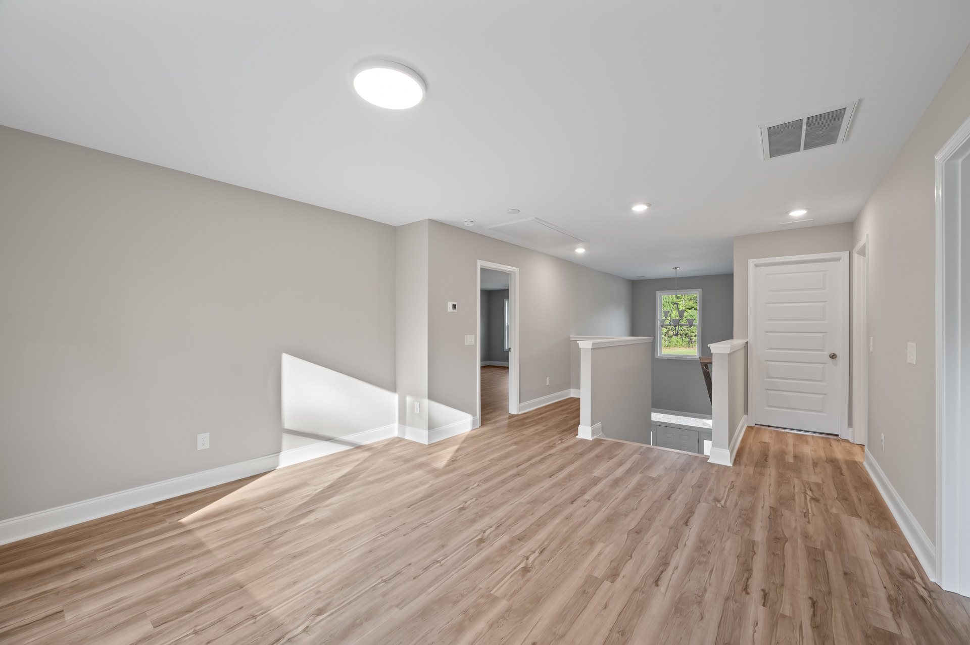 Wood flooring with white walls, white door featuring silver knob, ceiling vent, chandelier near window, close-up of ceiling light fixture
