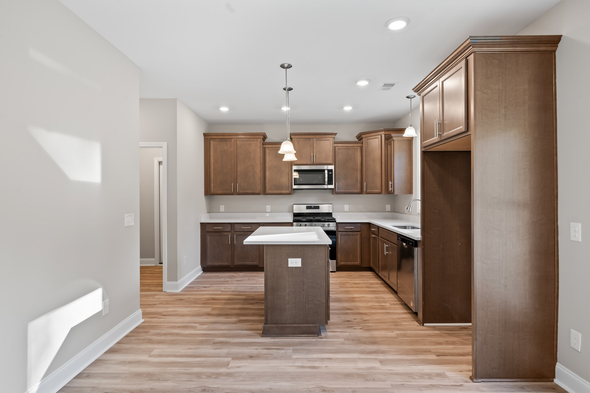 Kitchen with wood cabinets, white island countertop, tile flooring, built-in microwave with towel, sink, and modern lighting fixtures on white walls