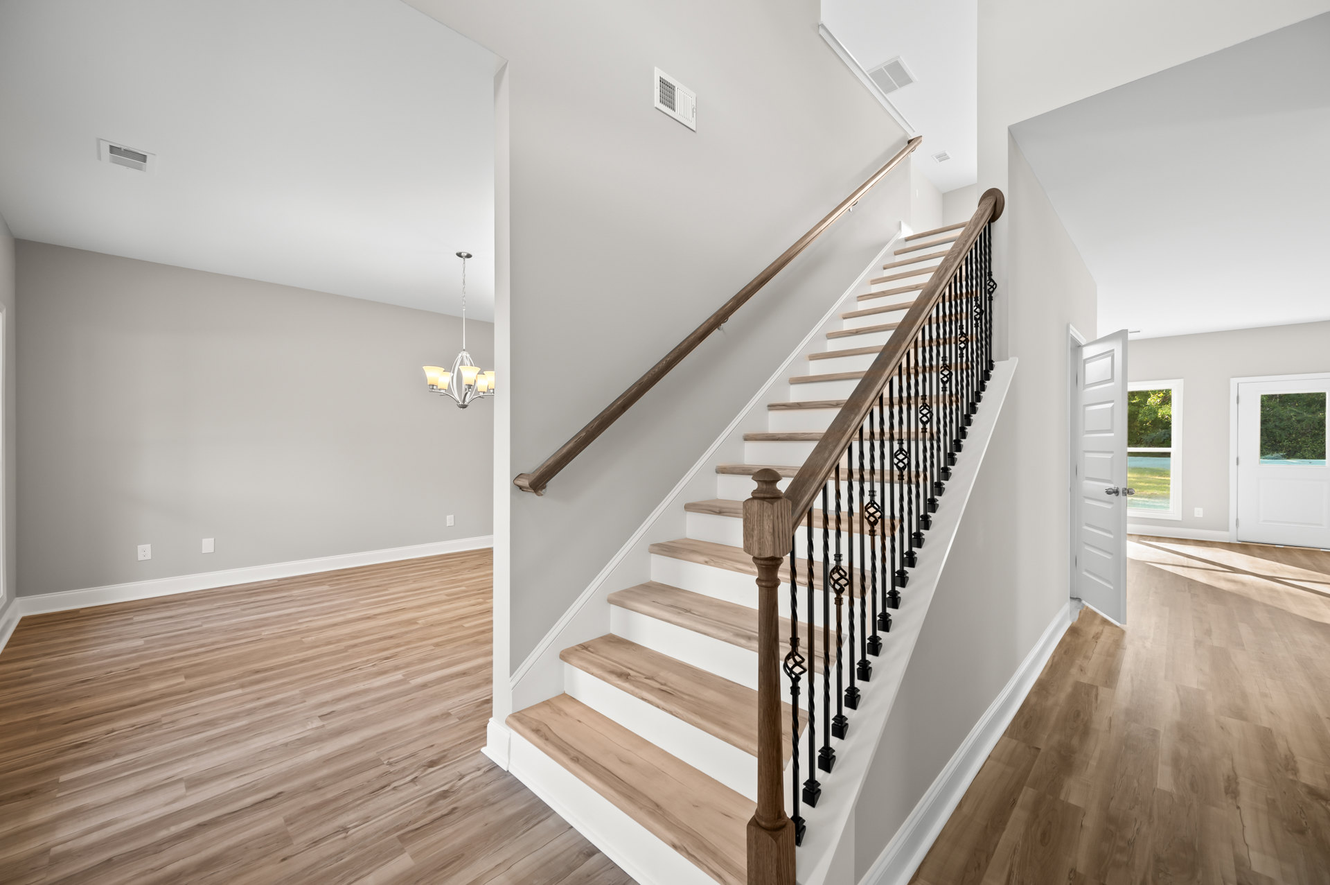 Wood and metal staircase with laminate flooring, white plaster walls, white door with window, metal handrail, and white wall vent
