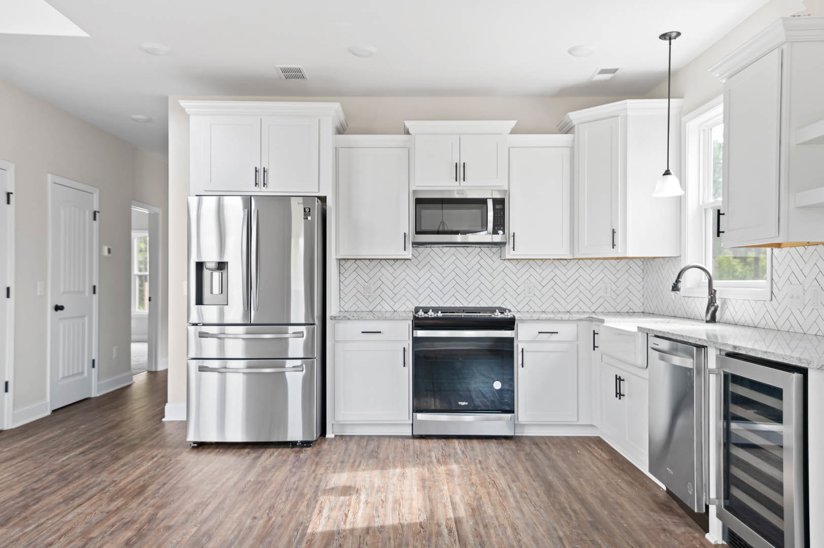 White shaker cabinets, stainless steel refrigerator and oven, quartz countertops, built-in microwave, pendant lamp, large window above sink, light hardwood flooring