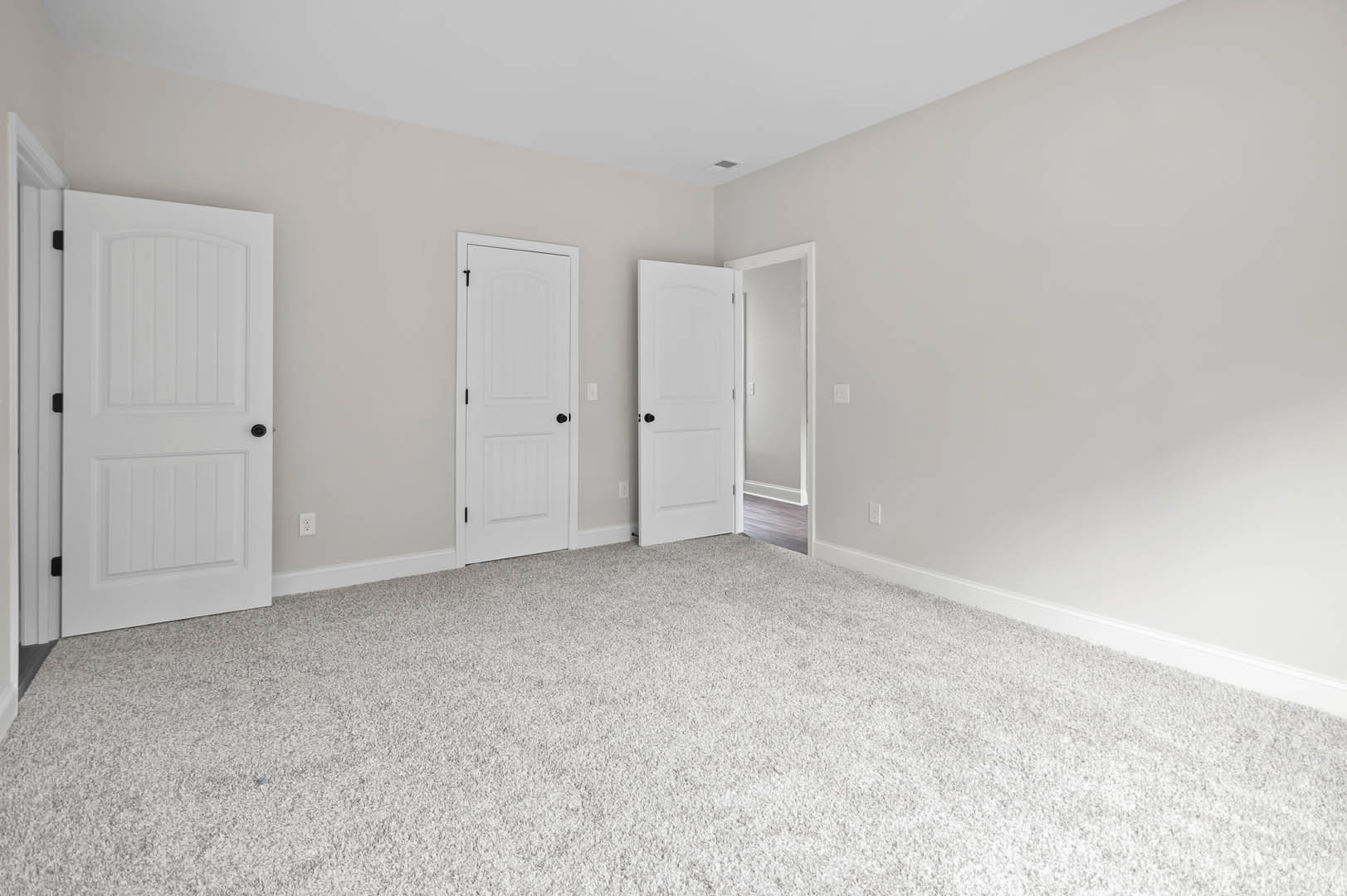 White carpeted room featuring white paneled doors with black knobs, white door frames, and a ceiling vent.