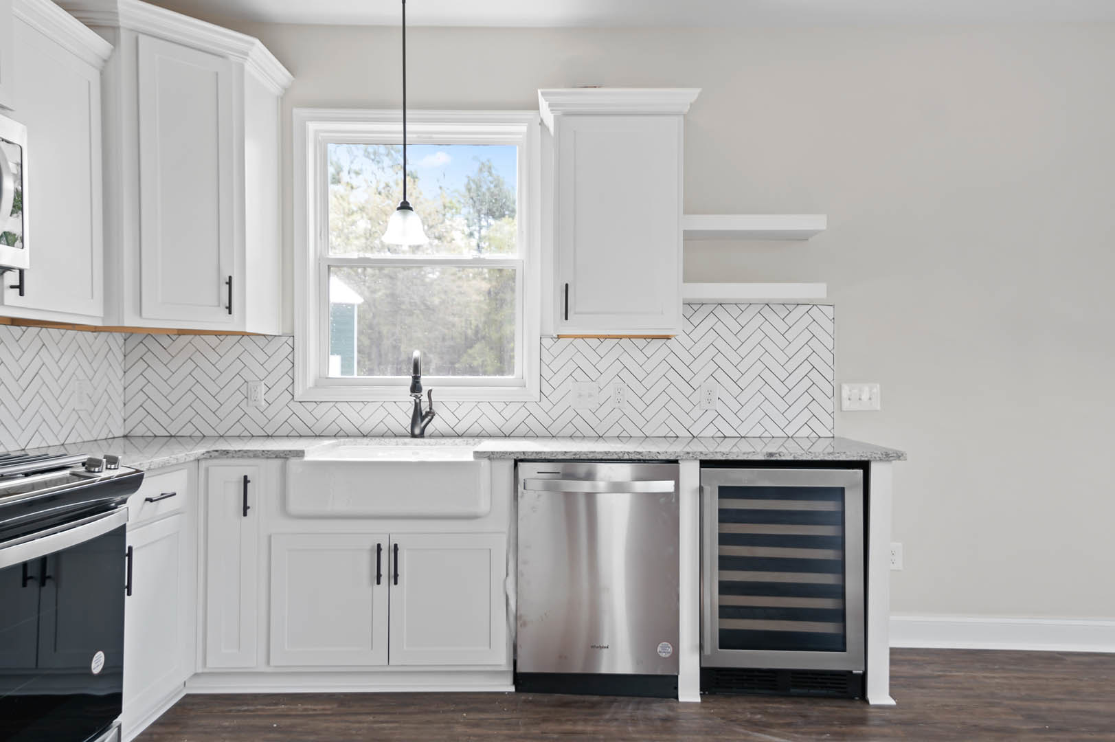 White shaker cabinets, stainless steel refrigerator, undermount sink set in light stone countertop, ceiling light fixture, black accent cabinet, window above sink, chrome faucet