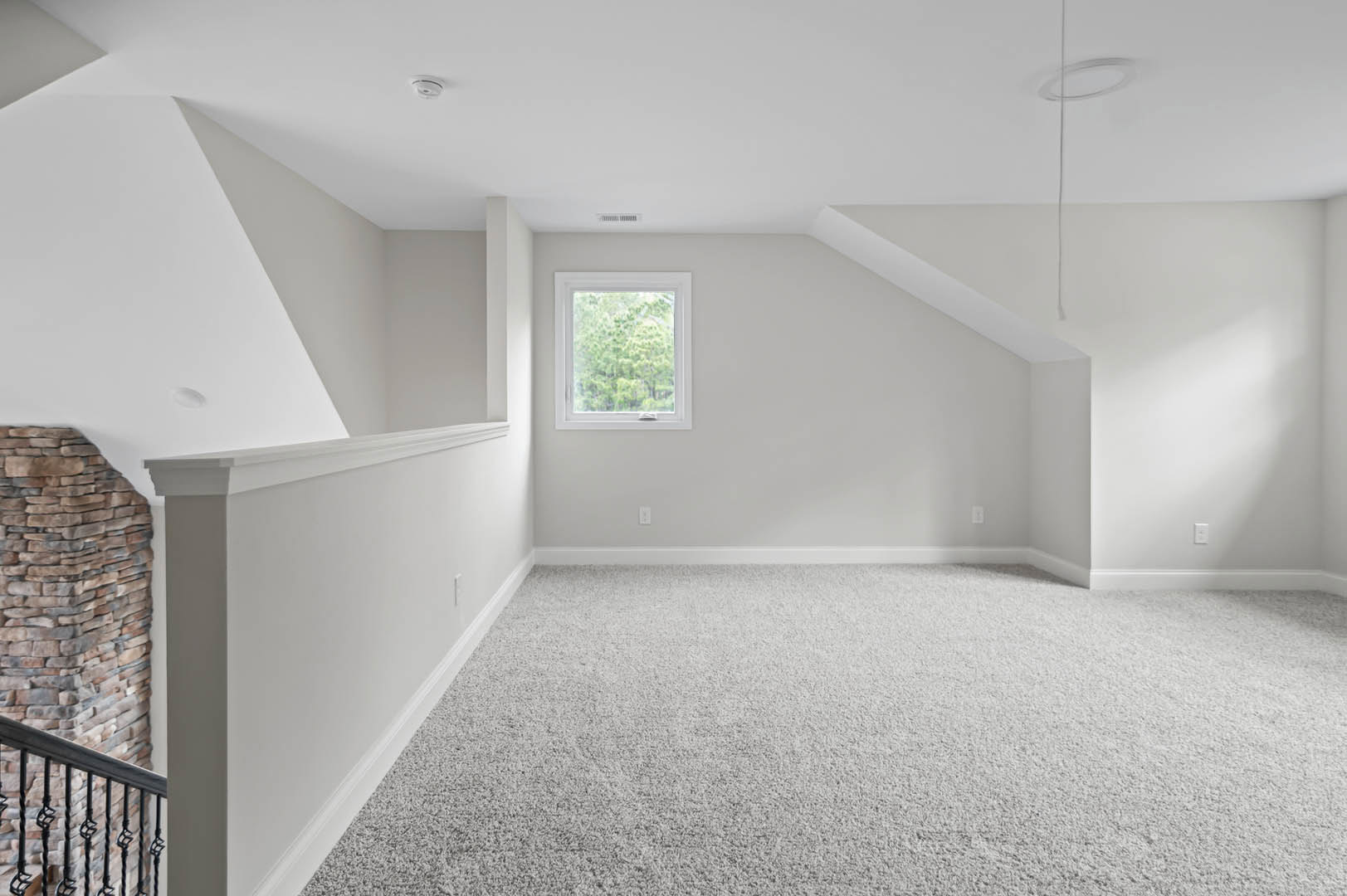 White carpeted room with a large window overlooking trees, stone accent wall, close-up of wooden staircase, white ceiling featuring a vent and crown molding.