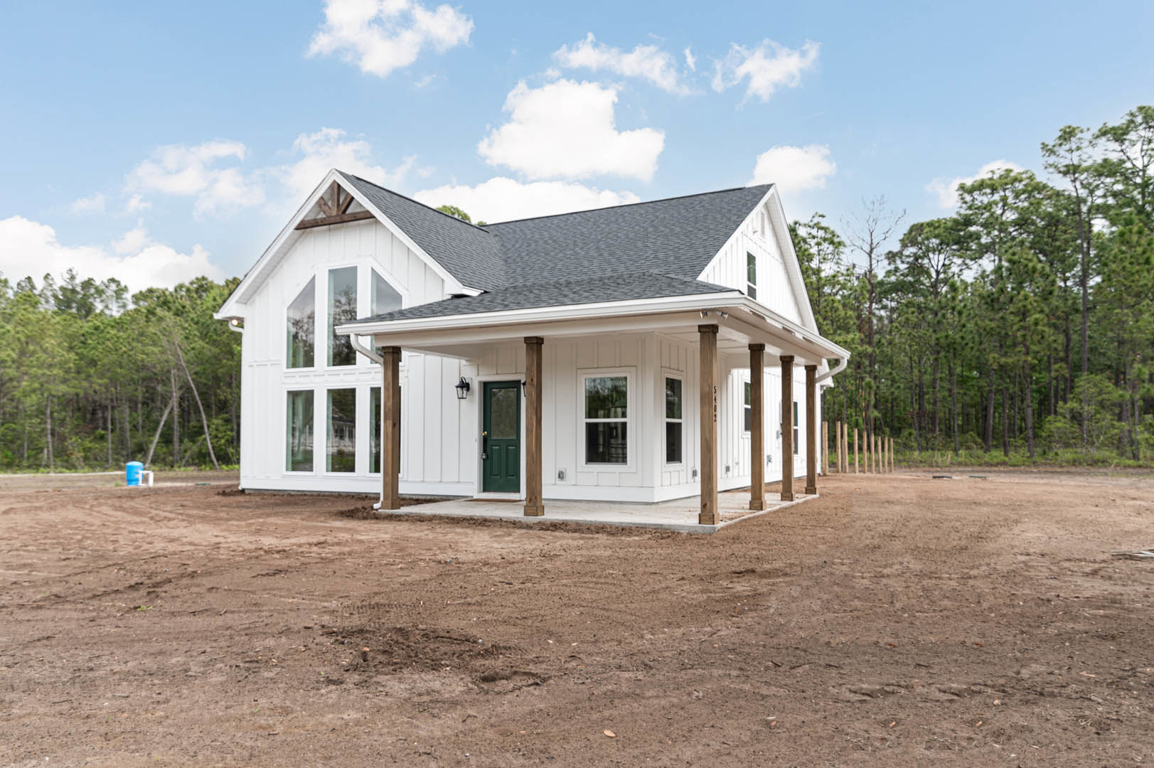 White house with green door featuring glass panel, white-framed window, dirt yard, blue sky with clouds above