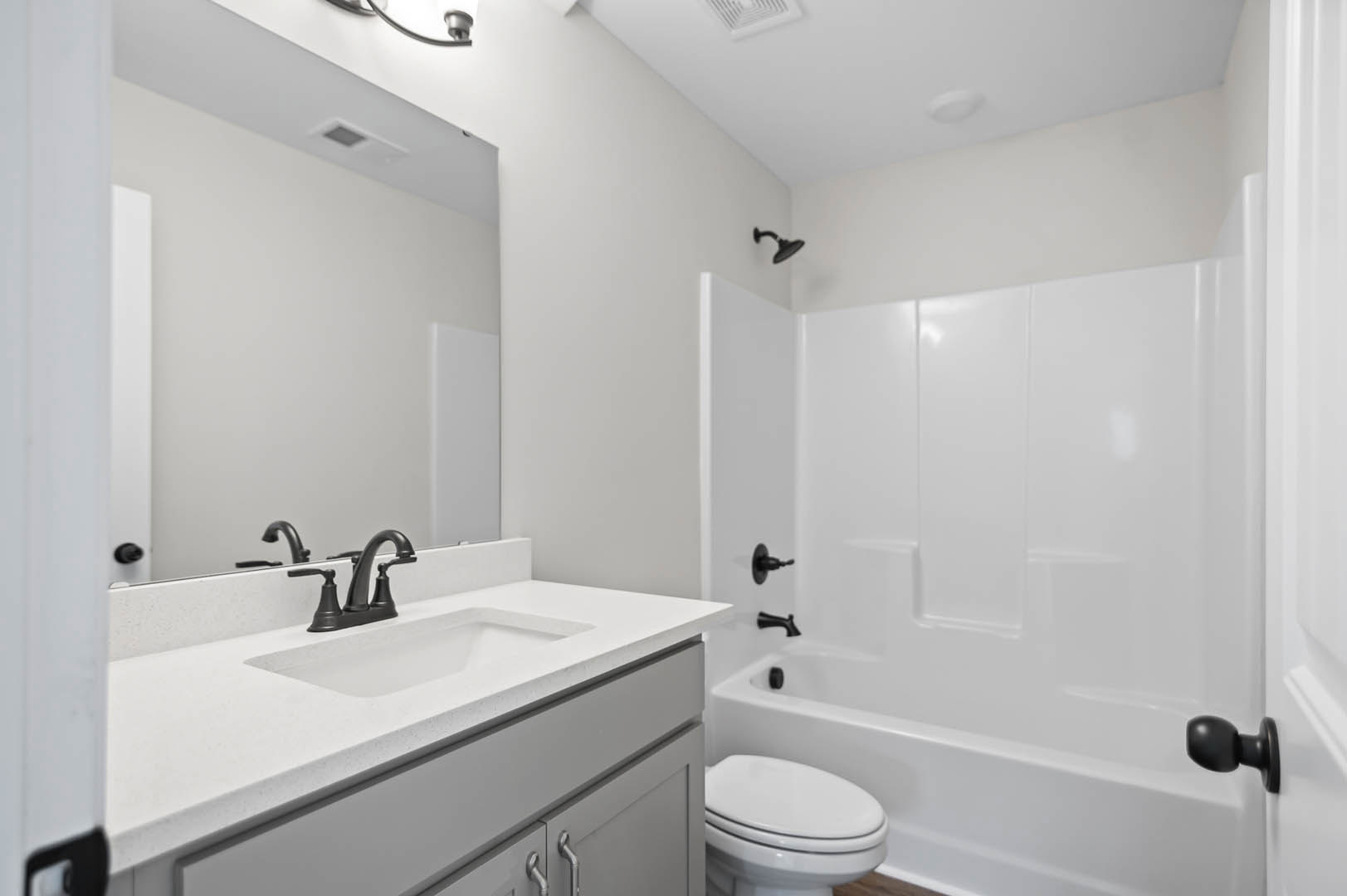 Modern bathroom featuring a tiled shower with glass door, white porcelain sink and chrome faucet, wall-mounted mirror, and closed toilet adjacent to neutral tile walls