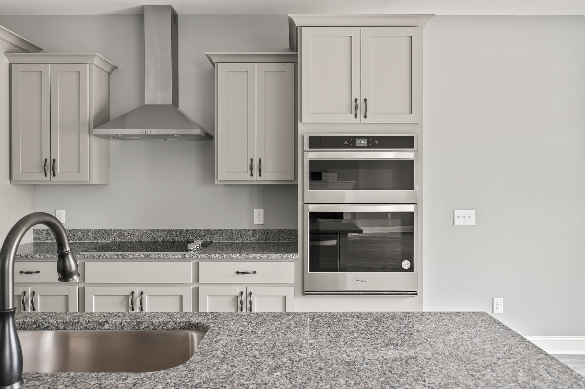 Granite countertops, two stainless steel ovens with glass windows, white cabinetry with black handles, metal plate detail, white light switch on wall, modern kitchen appliances and