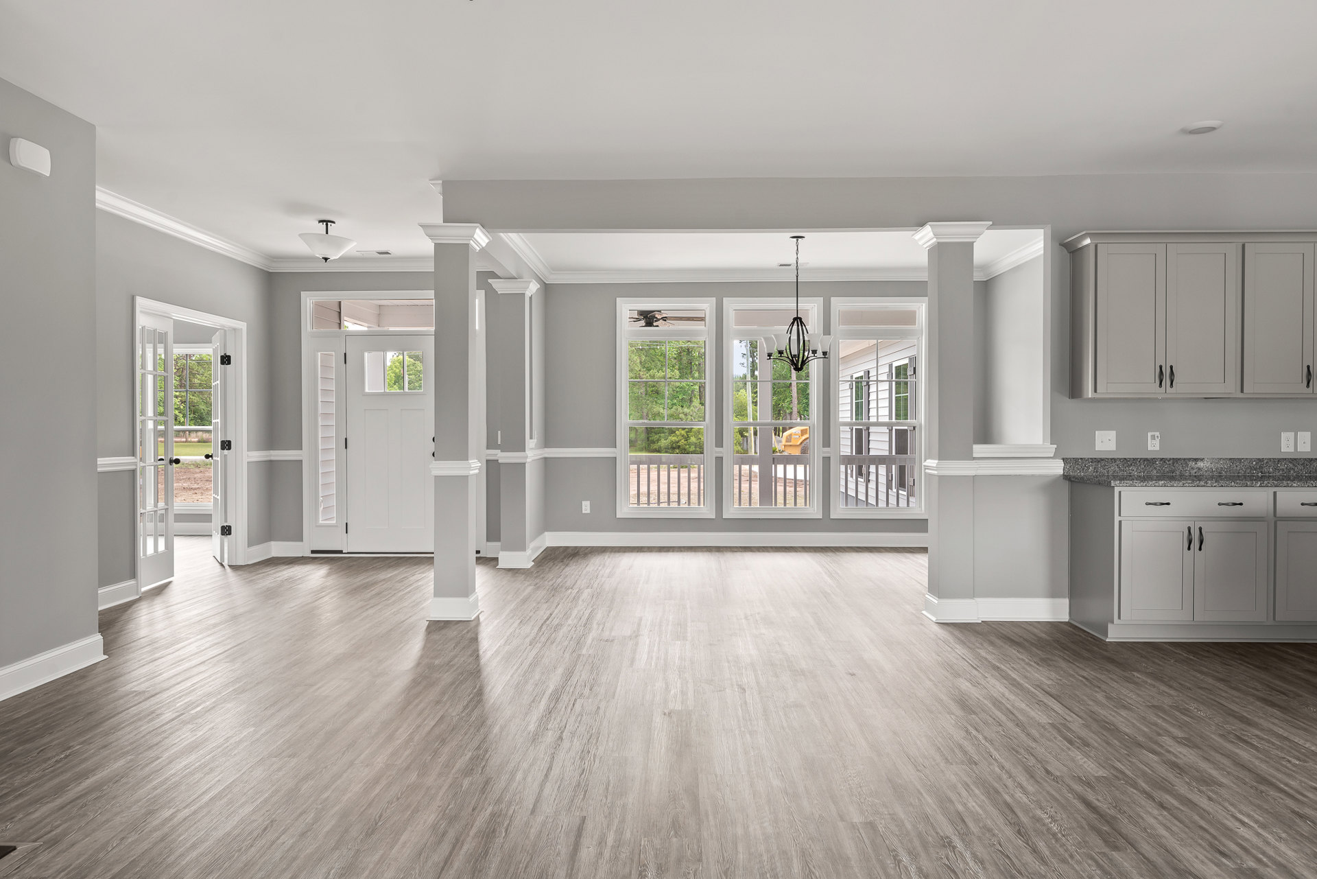Kitchen with light wood flooring, white cabinets with black handles, large window overlooking trees, and a wooden door