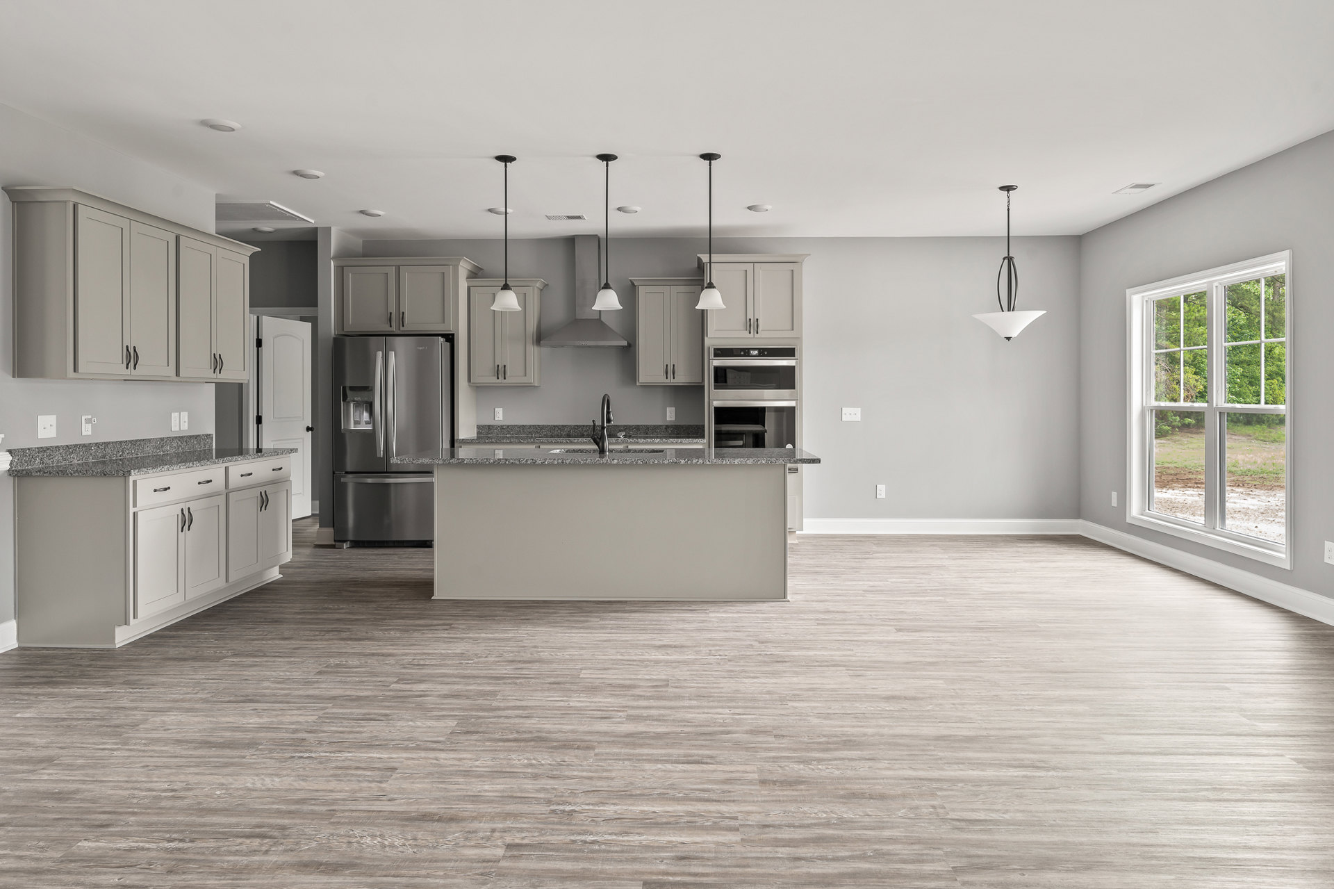 Open kitchen featuring a central island with quartz countertop, stainless steel refrigerator, wood flooring, white walls, undermount sink, black pendant lamp, and window