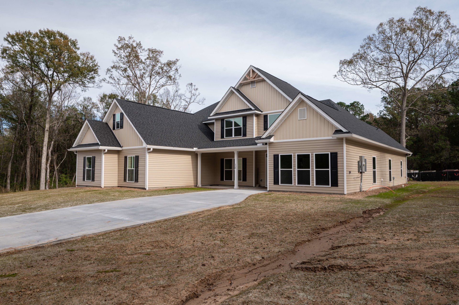 Two-story home with white-framed windows, covered porch, paved driveway, green lawn, mature trees, and Robert Frost Farm visible in the background
