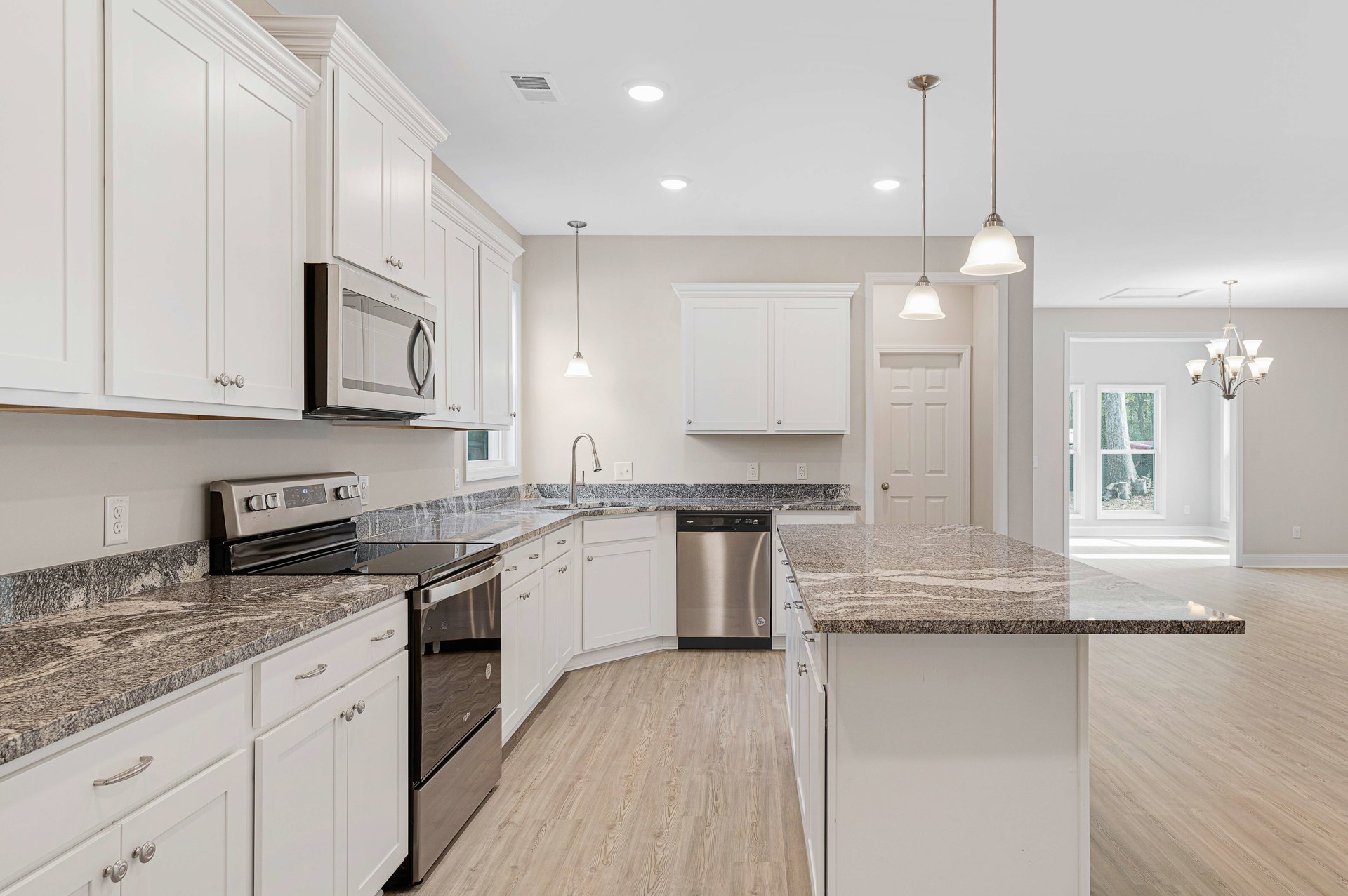 Granite countertops, wood flooring, white cabinetry with silver knobs, stainless steel refrigerator, white microwave with glass door, metal towel bar mounted on white wall