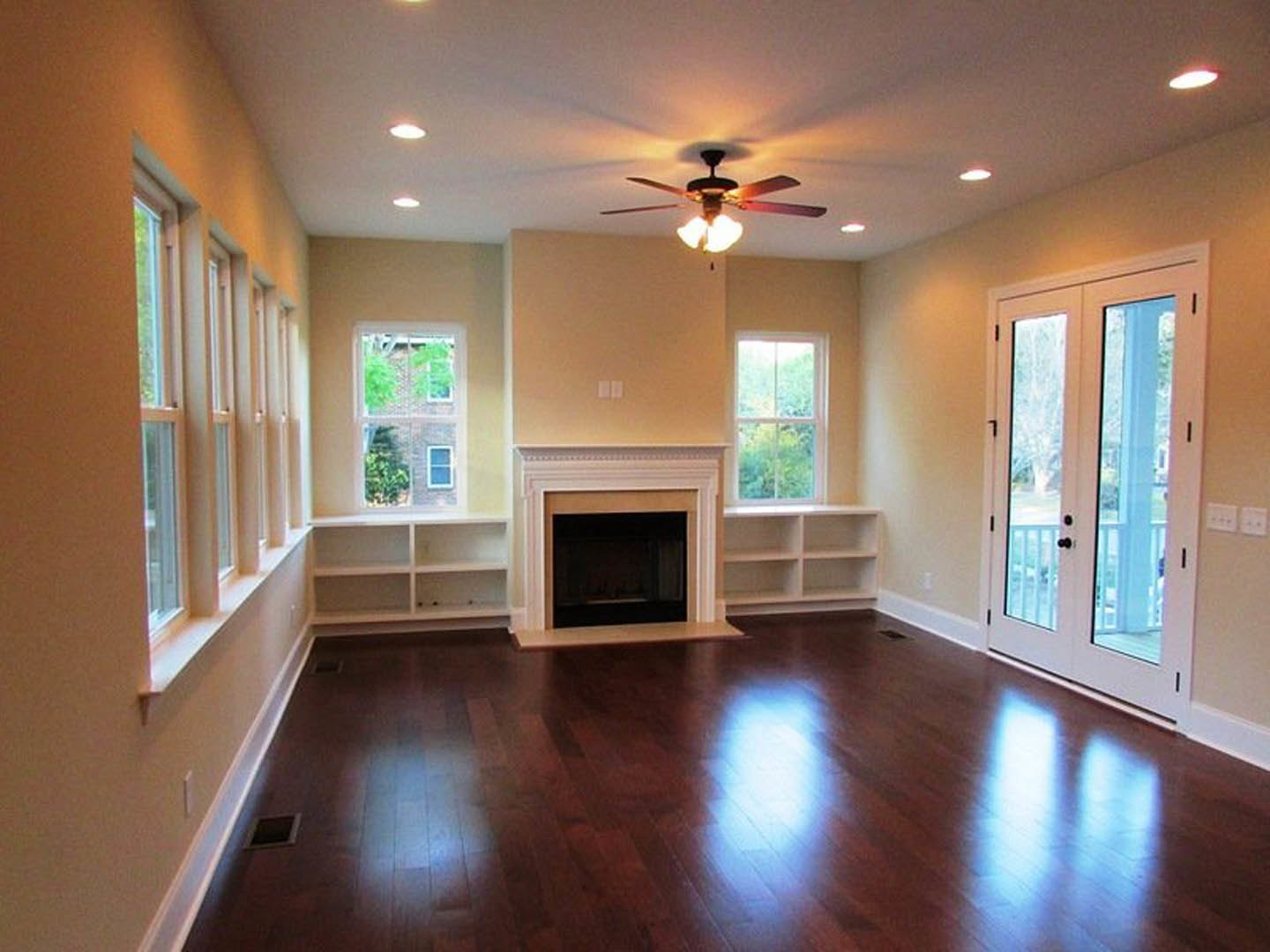 Living room with white-framed fireplace, hardwood floors, ceiling fan with light, white trim molding, and large window