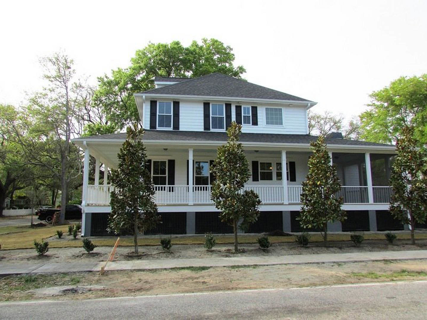 Two-story house with white-framed windows, covered front porch, and mature trees in landscaped yard