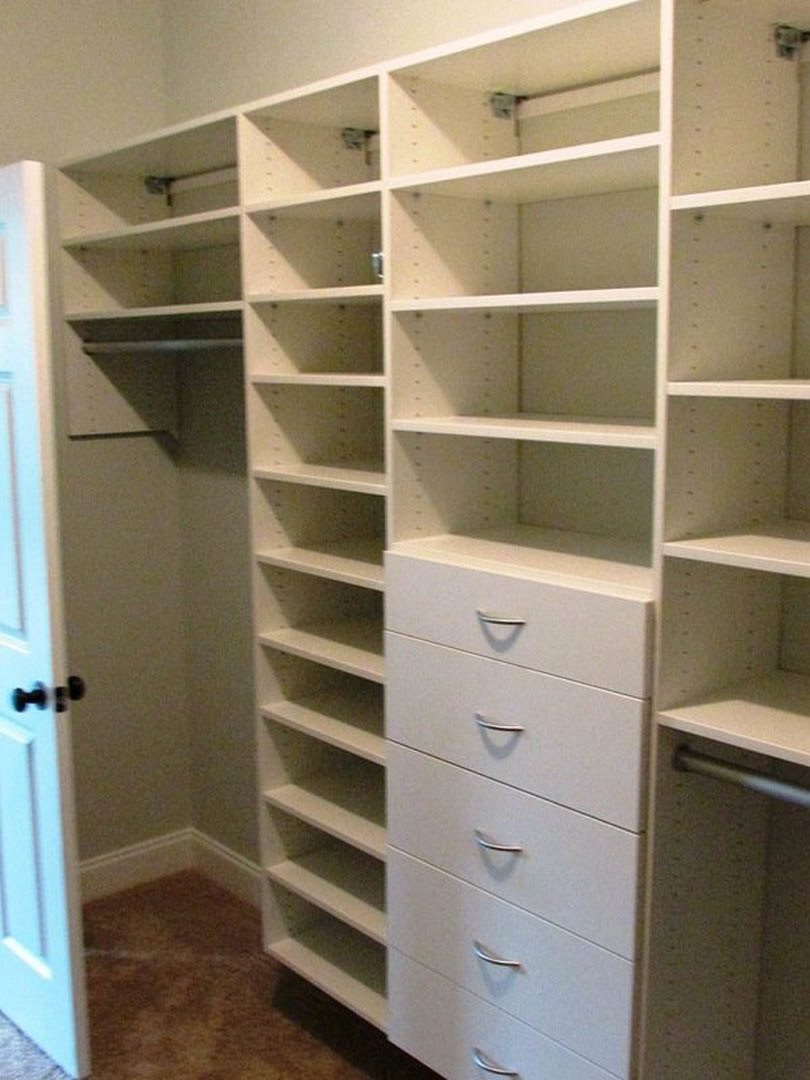 Walk-in closet featuring built-in white shelves and drawers, light-colored walls, and organized cabinetry