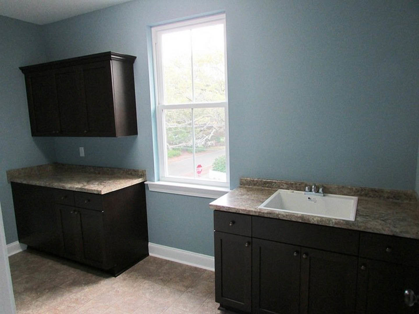 Bathroom with dark wood cabinets, black countertop, white sink and faucet, white-framed window, tile walls, and modern cabinetry.