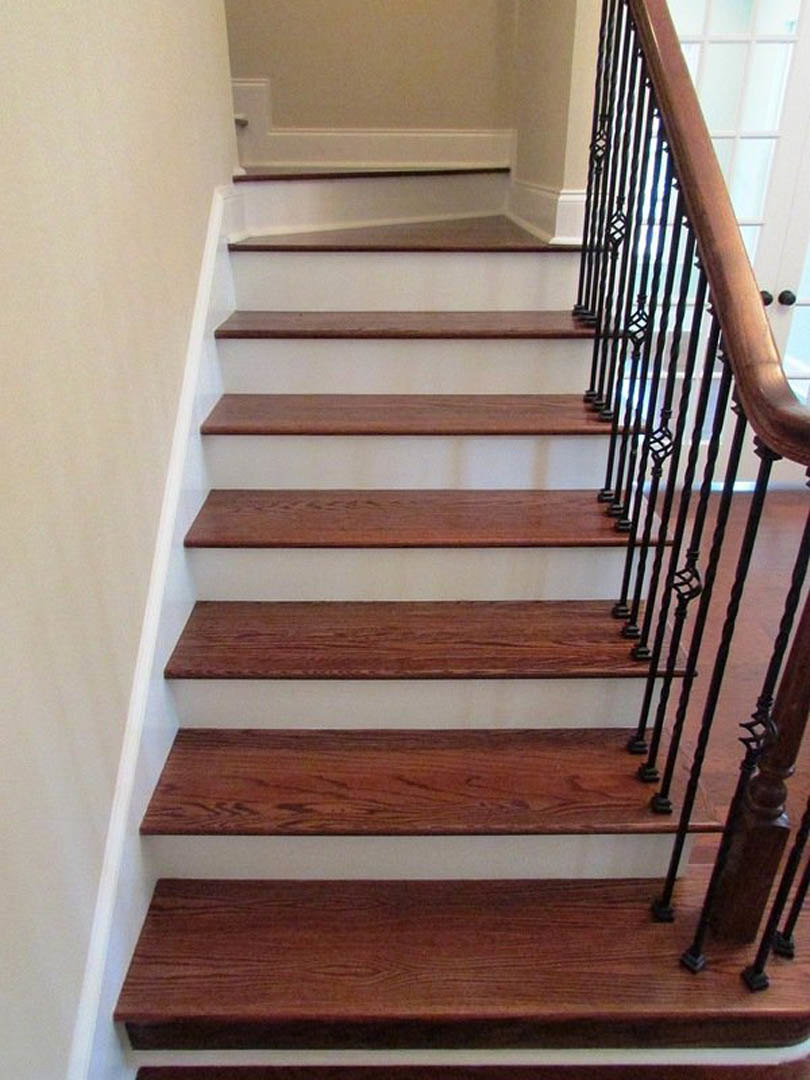 Staircase with natural wood steps and sleek black metal railing, adjacent to a white wall in a modern interior