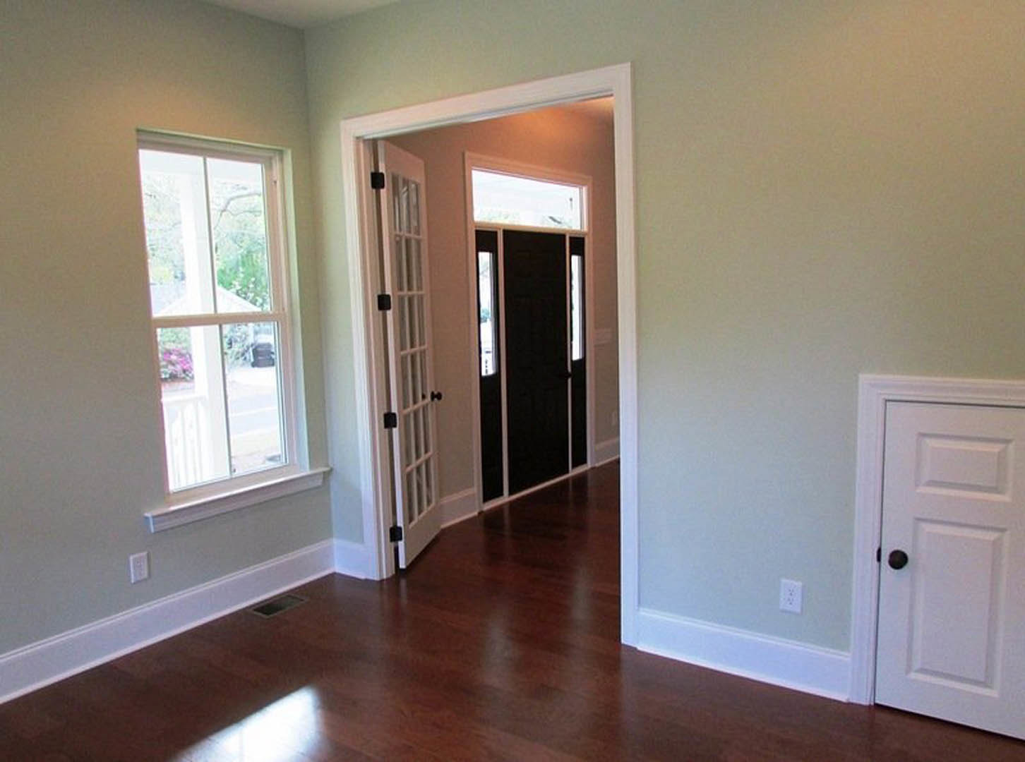Hallway with light wood flooring, white walls, and a black door featuring glass window panels and a silver handle