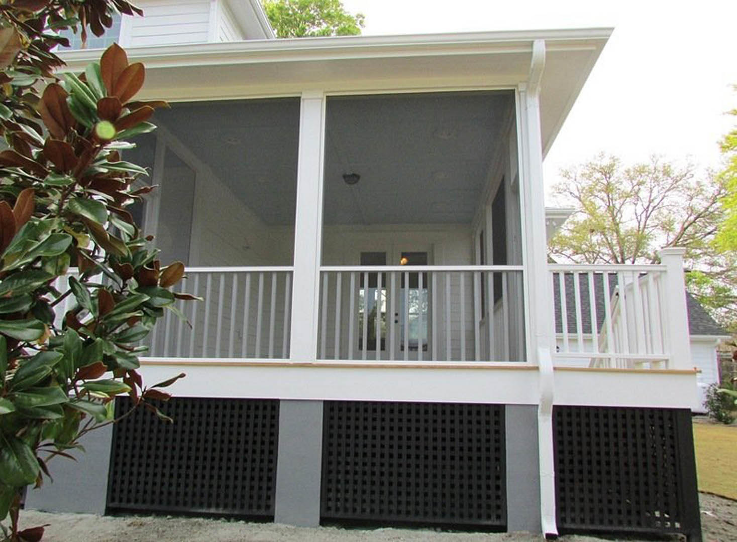 Covered porch with screened enclosure, white siding, wood decking, and leafy green plants in foreground