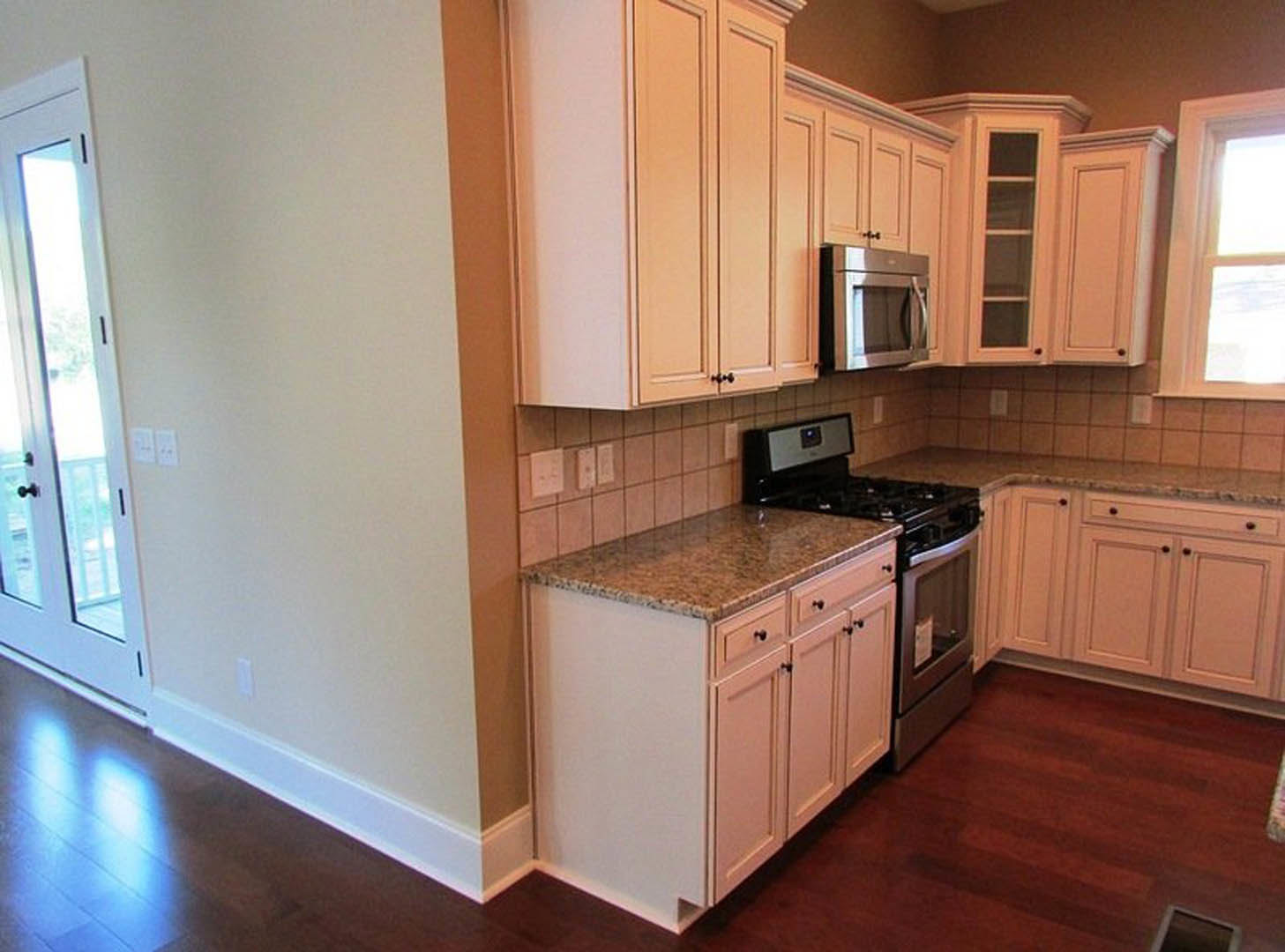 White kitchen cabinets with granite countertops, stainless steel microwave, light switch on wall, window, and tiled floor