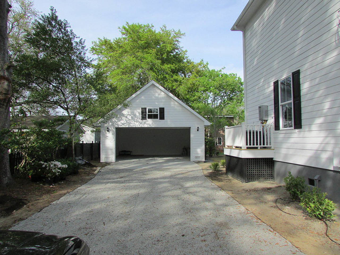 Two-car garage with white paneled door, concrete driveway, mature trees, and light-colored siding