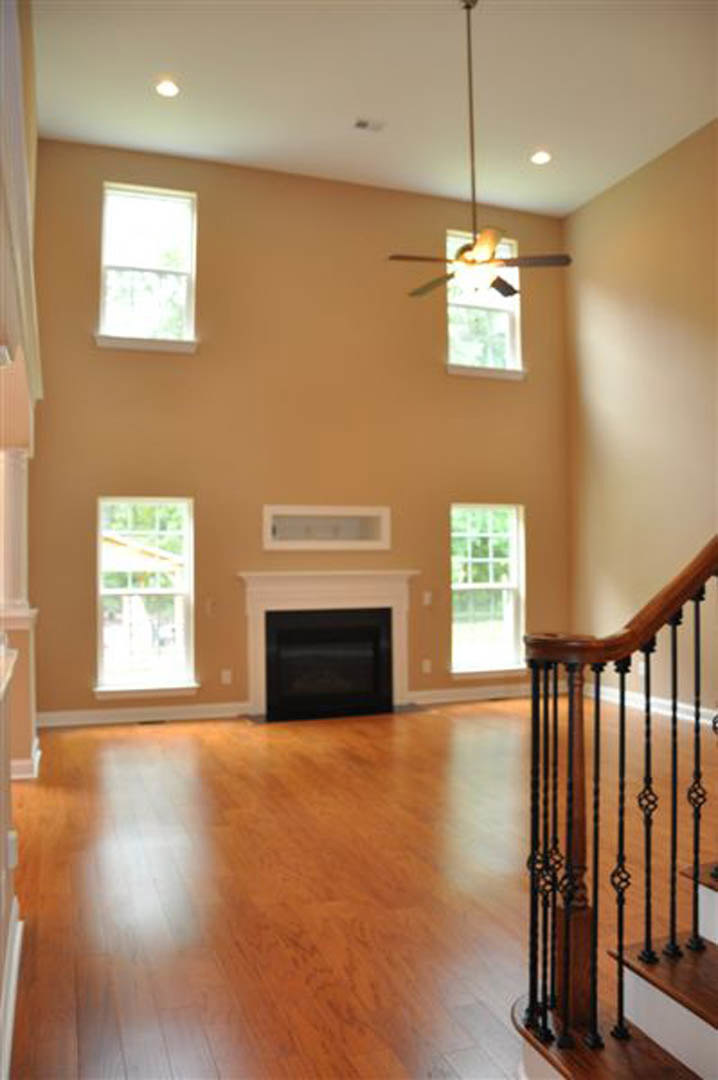 Living room with hardwood floors, white-framed window, black metal railing, and a central fireplace surrounded by light-colored molding