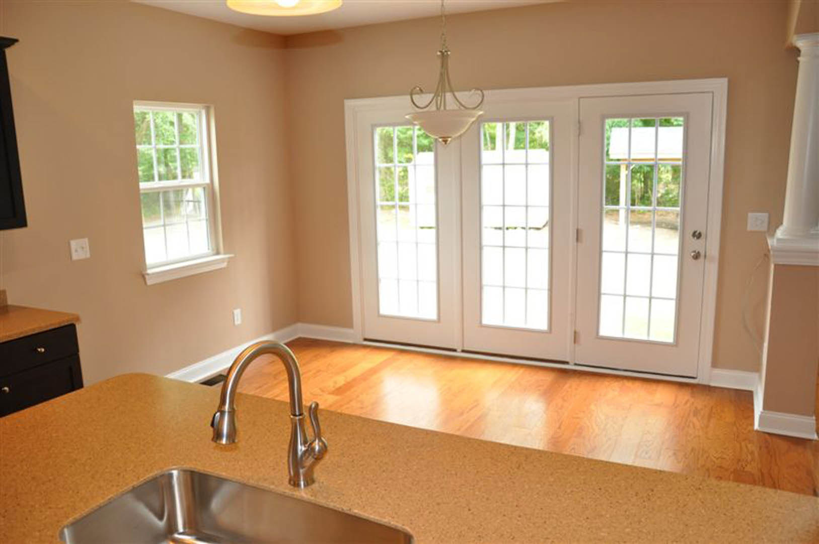 White kitchen with glass-paneled double doors, marble countertop, stainless steel faucet, white cabinetry, and wall outlet.