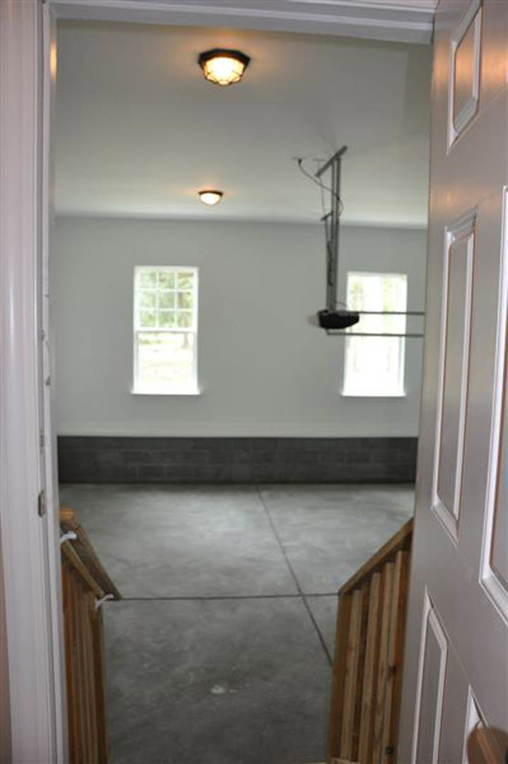 Entryway with concrete floor, wooden gate, and plaster walls; window reveals leafy trees outside; brick accent wall and decorative molding visible.