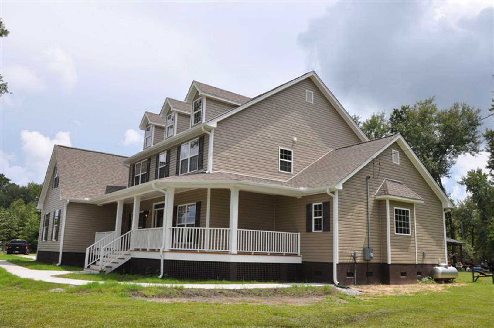 Two-story home with covered porch, white railings, multi-pane windows, manicured lawn, and a black truck parked in front